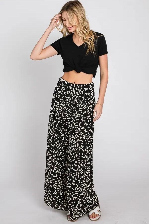 Woman wearing high-waisted black wide leg pants with white irregular Dalmatian spots and a knotted black crop top