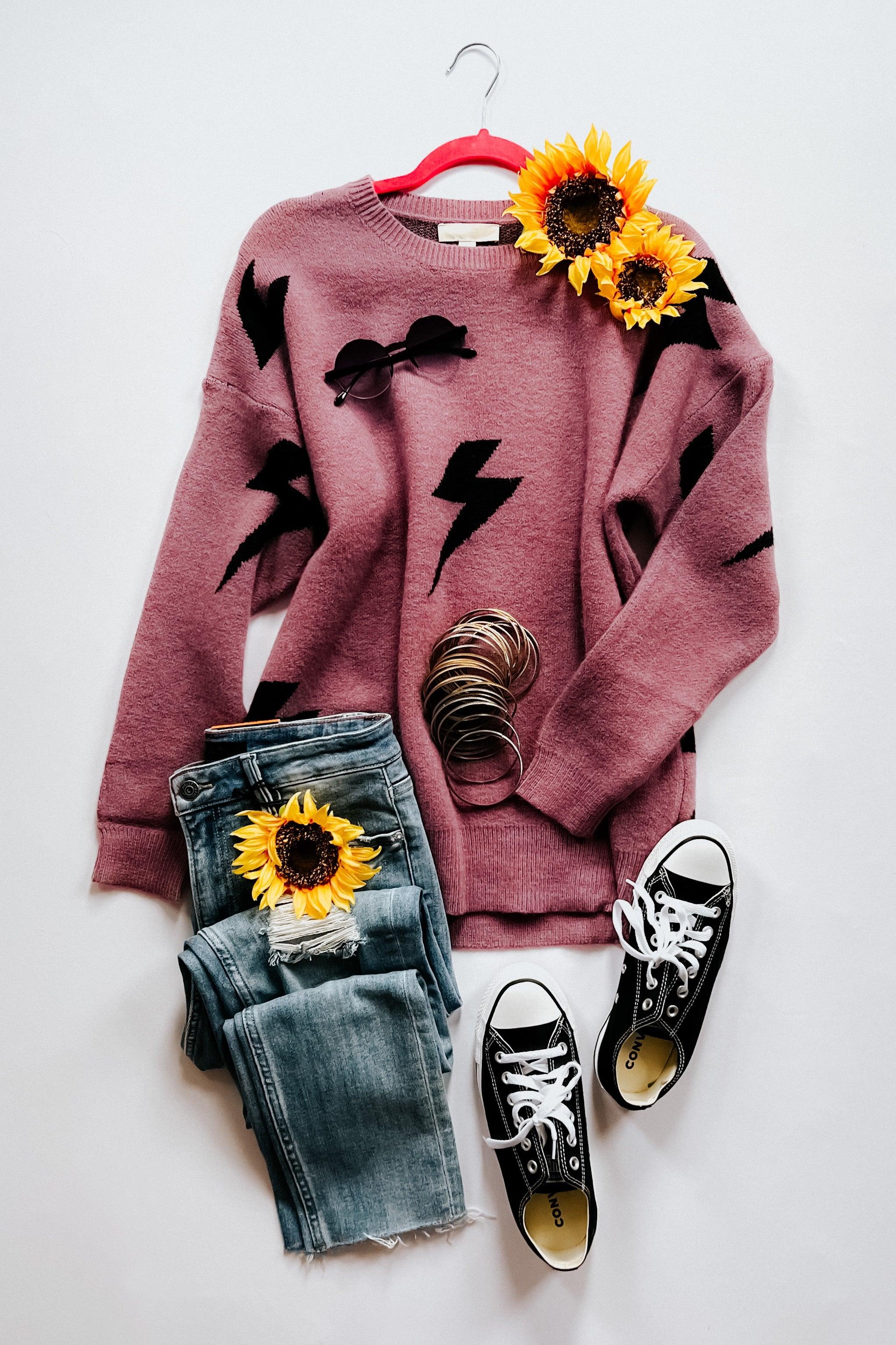 Flatlay of a purple sweater with black lightning bolts, blue jeans, black converse shoes and sunflowers on a white background