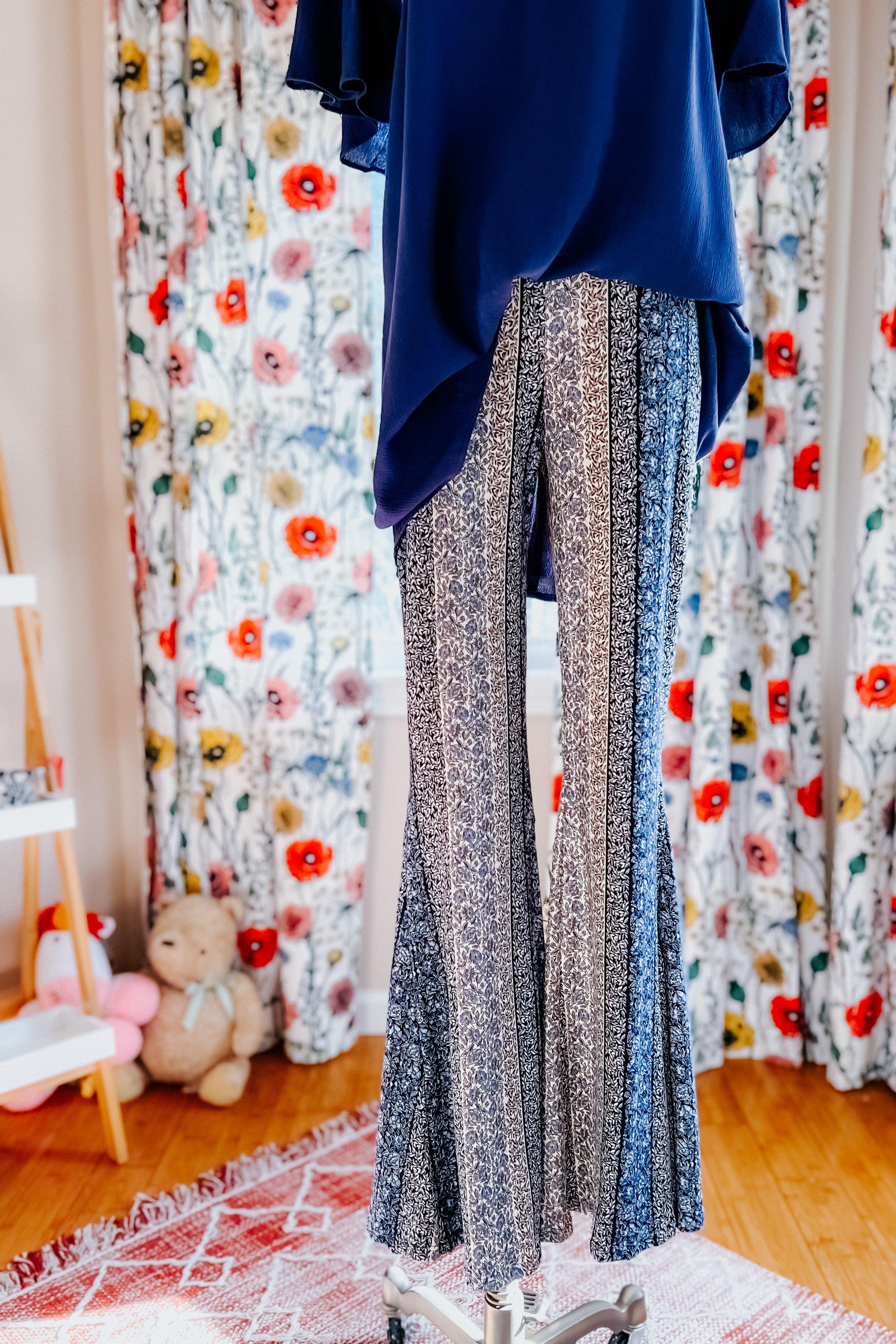Fleetwood Floral Bell Bottoms in navy featuring vertical detailed floral stripes, displayed on a mannequin with a navy tunic in a bright room with floral curtains.
