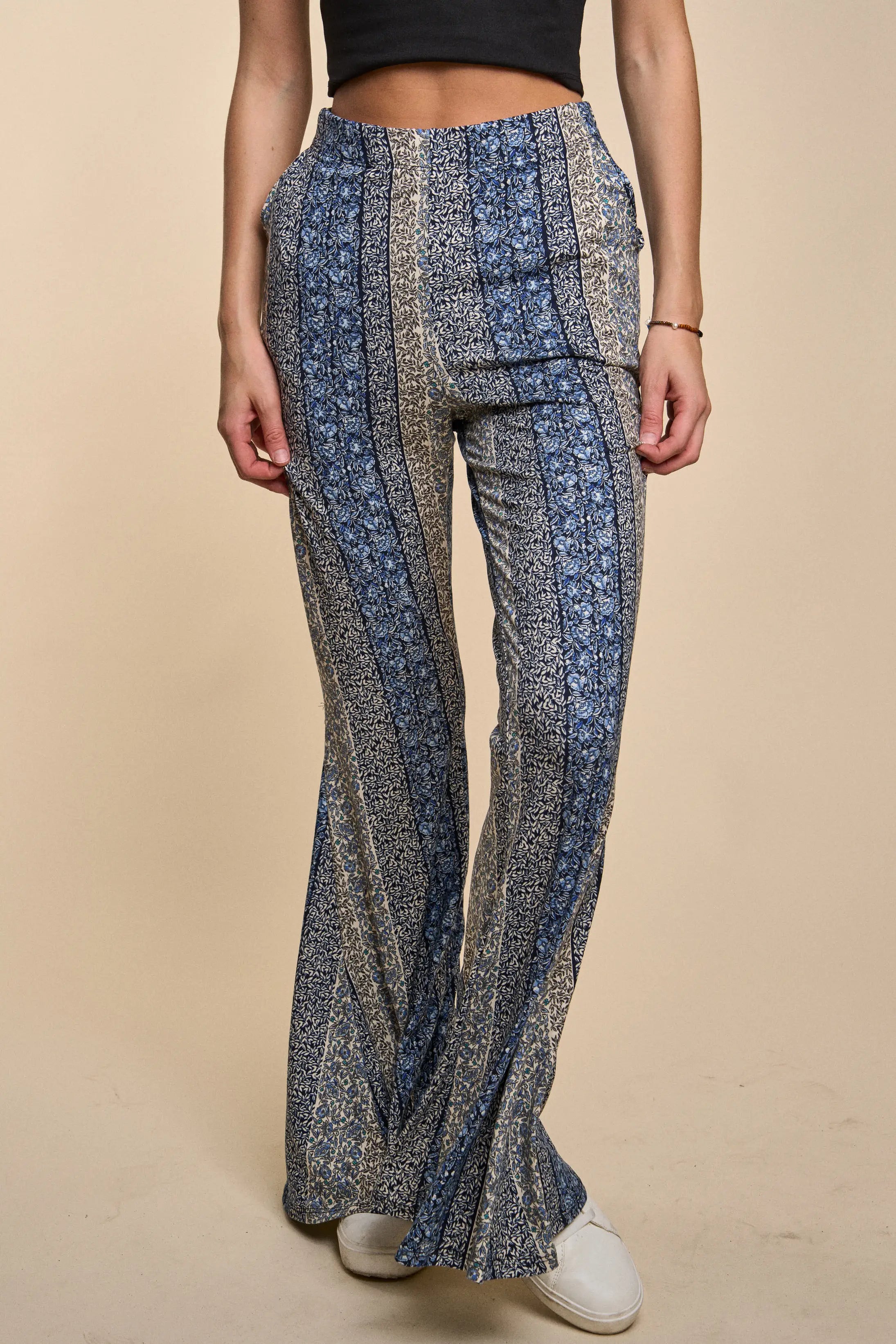 Fleetwood Floral Bell Bottoms in navy with intricate vertical floral stripes, styled with white shoes and a cropped black top on a warm beige backdrop