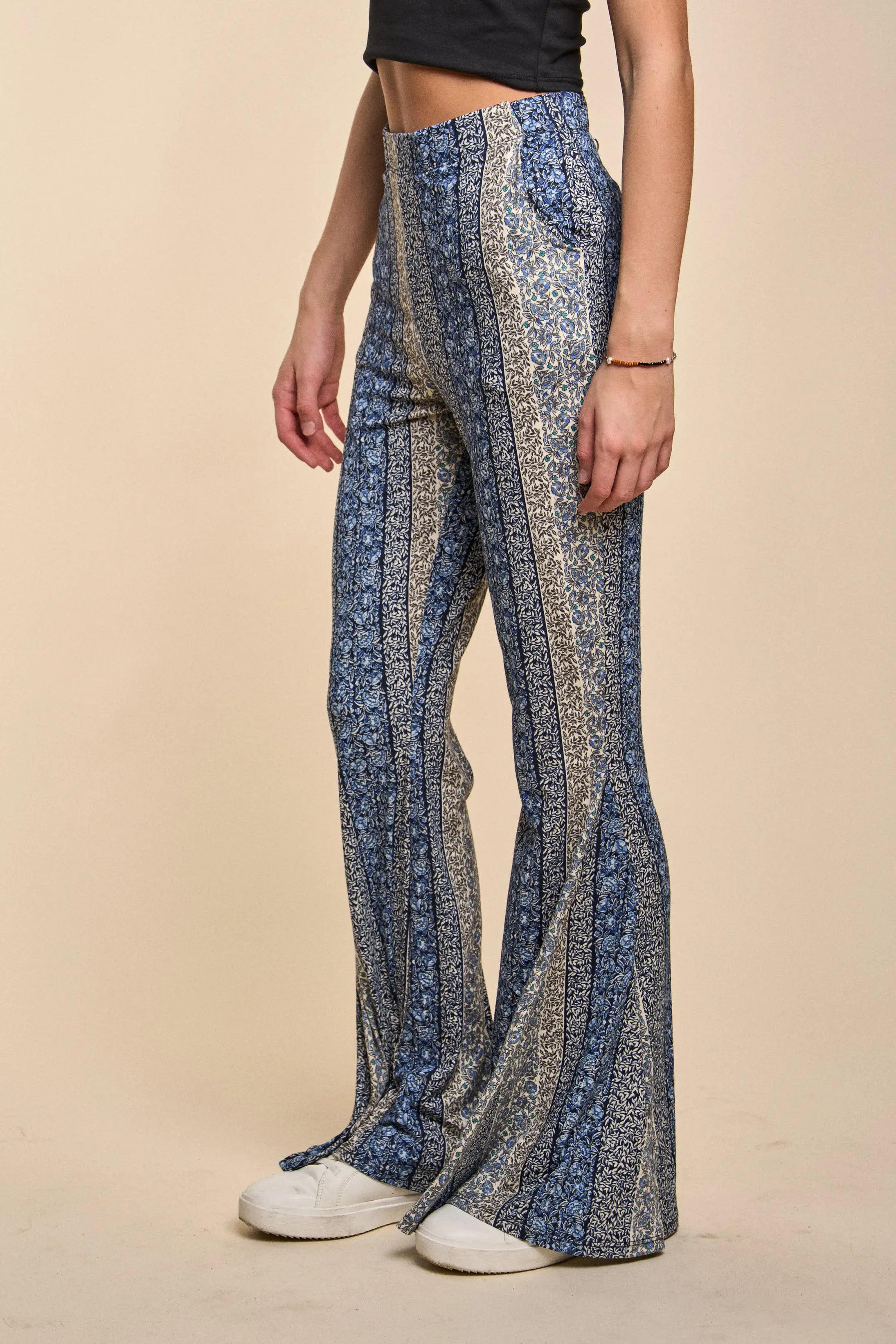 Fleetwood Floral Bell Bottoms in navy with vertical stripes and mixed floral patterns, styled with white sneakers and a black cropped top on a beige background