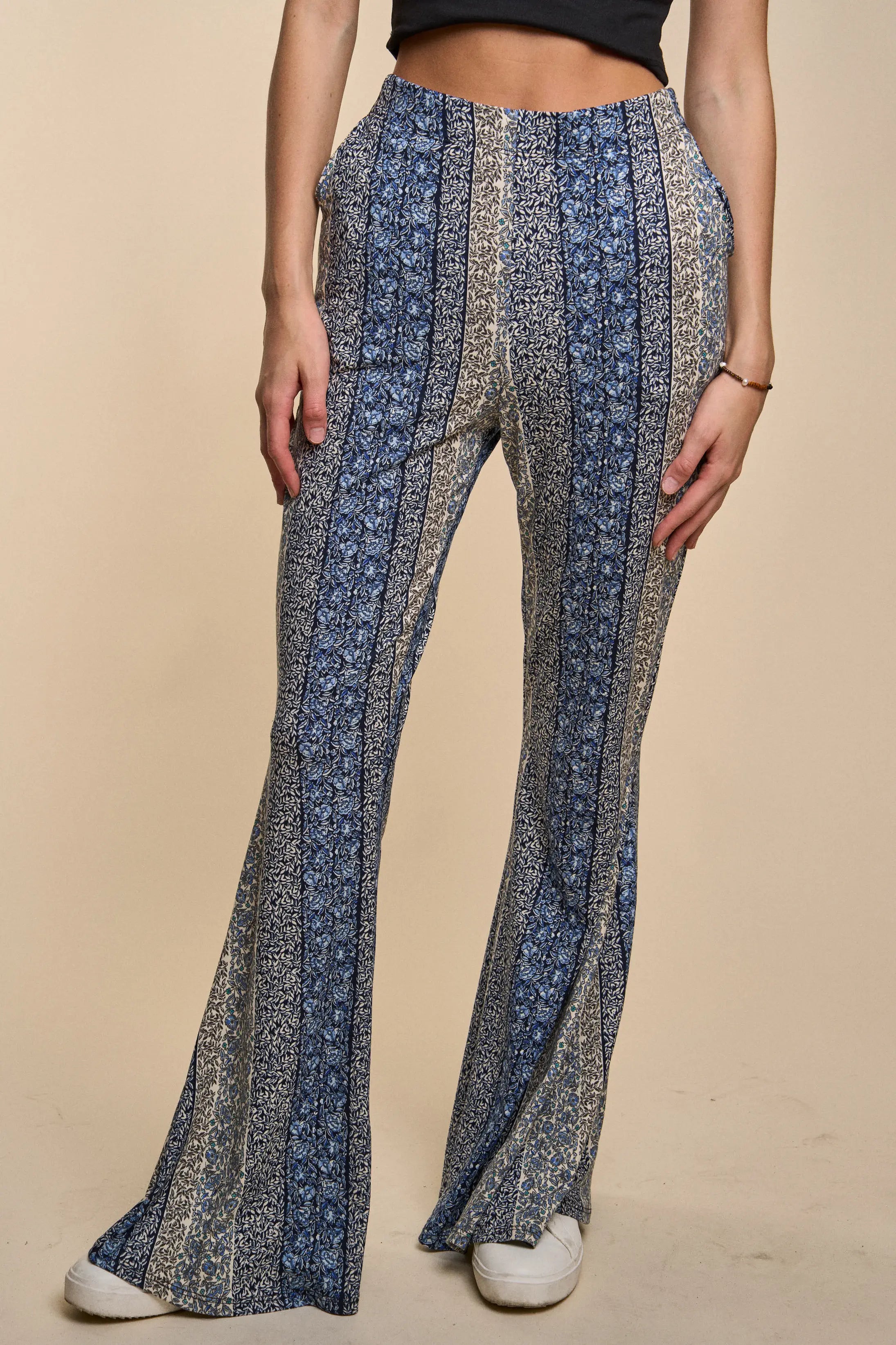 Fleetwood Floral Bell Bottoms featuring vertical blue and beige floral stripes styled with white sneakers and a black cropped top on a neutral background