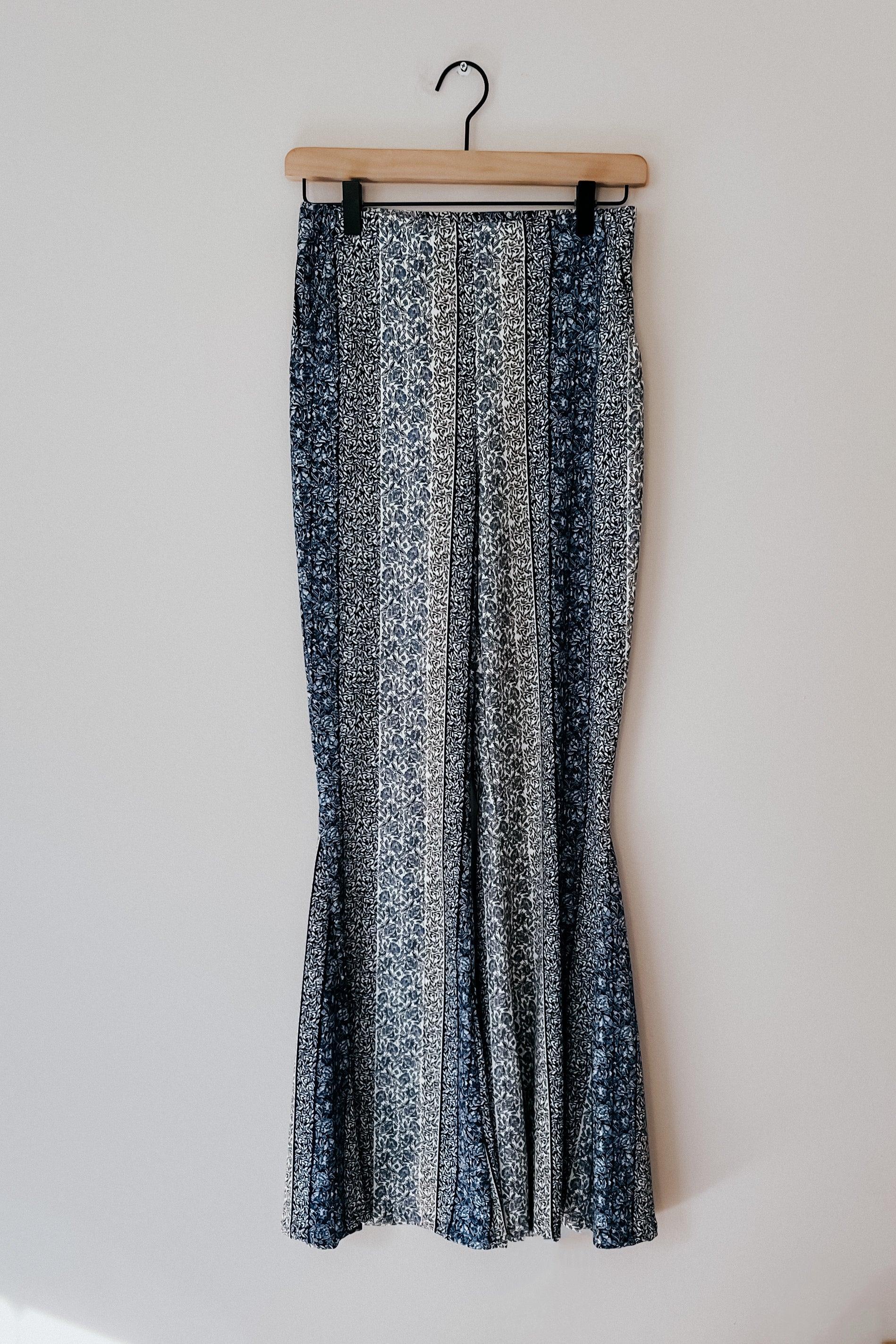 Fleetwood Floral Bell Bottoms in navy featuring alternating vertical floral patterns hanging on a wooden hanger against a plain light gray background