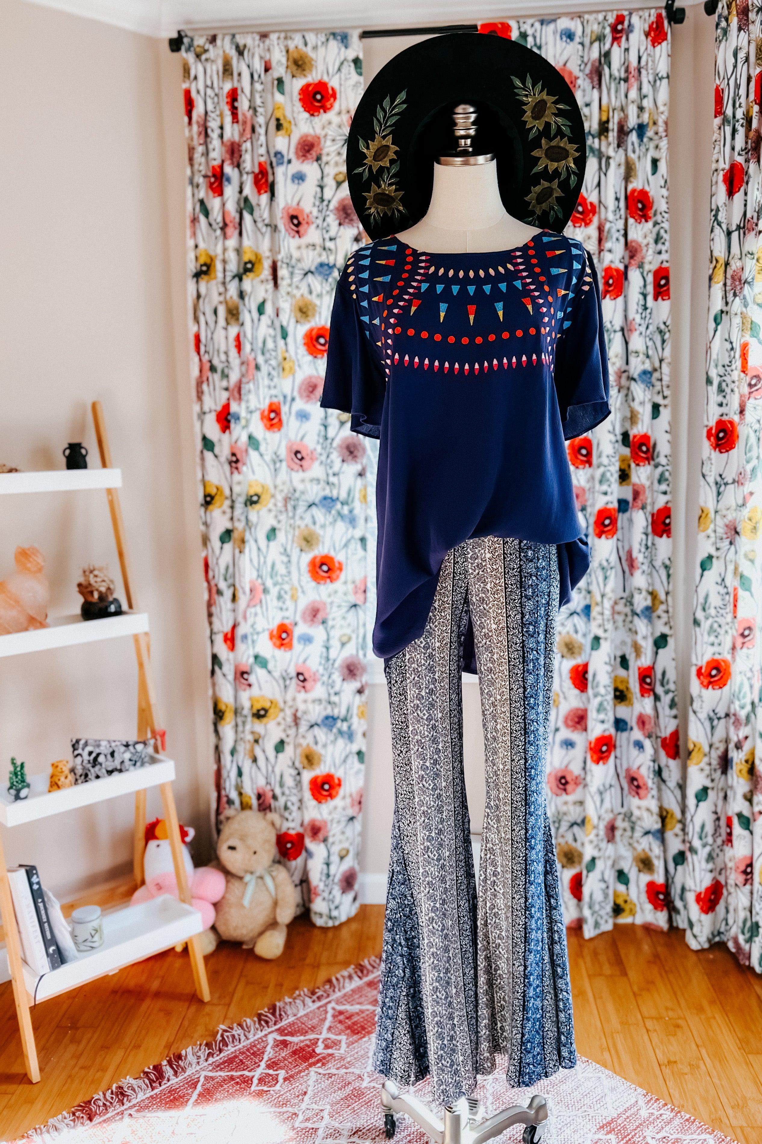 Fleetwood Floral Bell Bottoms in navy with delicate vertical patterns, styled on a mannequin with a navy top and black floral hat in a cozy room setting