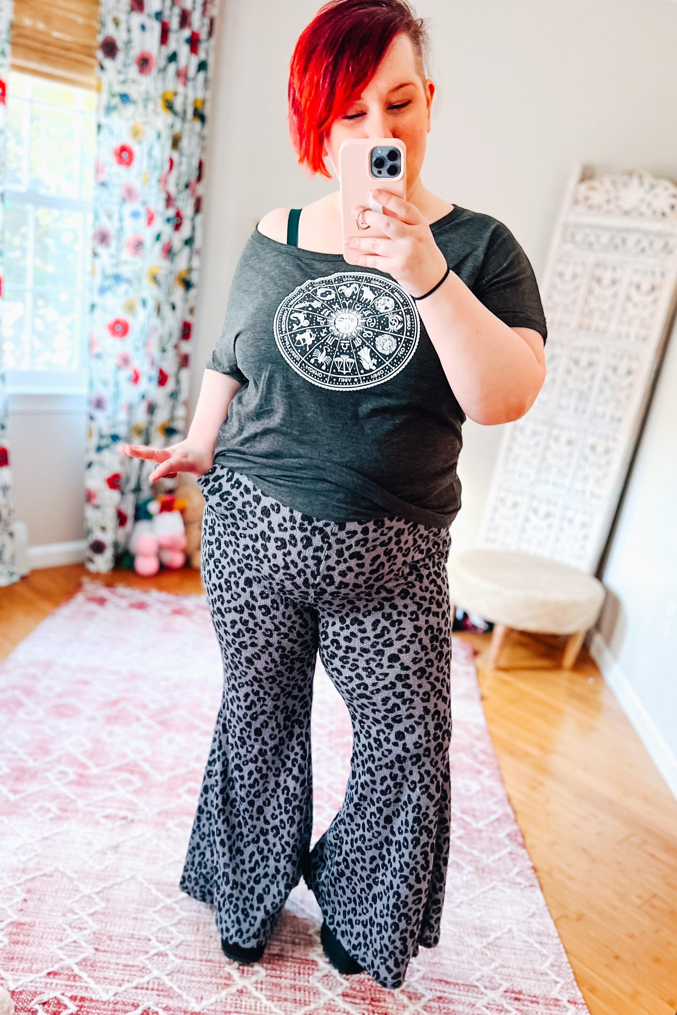 Woman wearing high-rise black and blue leopard print flared pants with a loose dark gray graphic t-shirt indoors