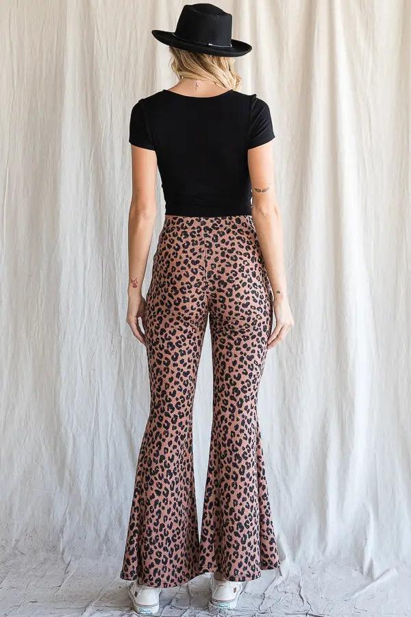 Woman wearing mocha leopard print flared pants paired with a fitted black short sleeve top and black hat against neutral backdrop
