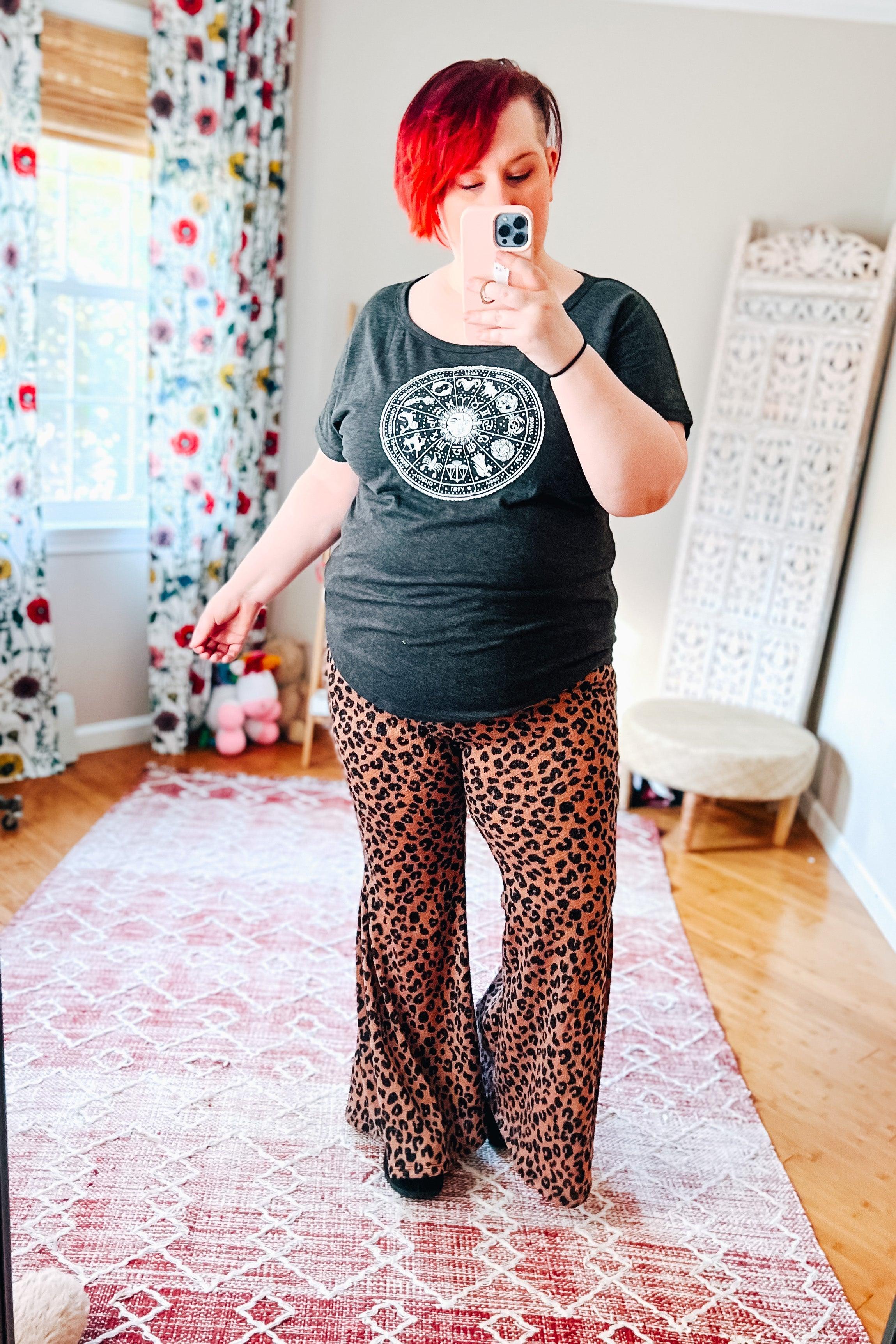 Woman taking selfie wearing mocha leopard print bell bottoms with black astrology graphic t-shirt in bright room