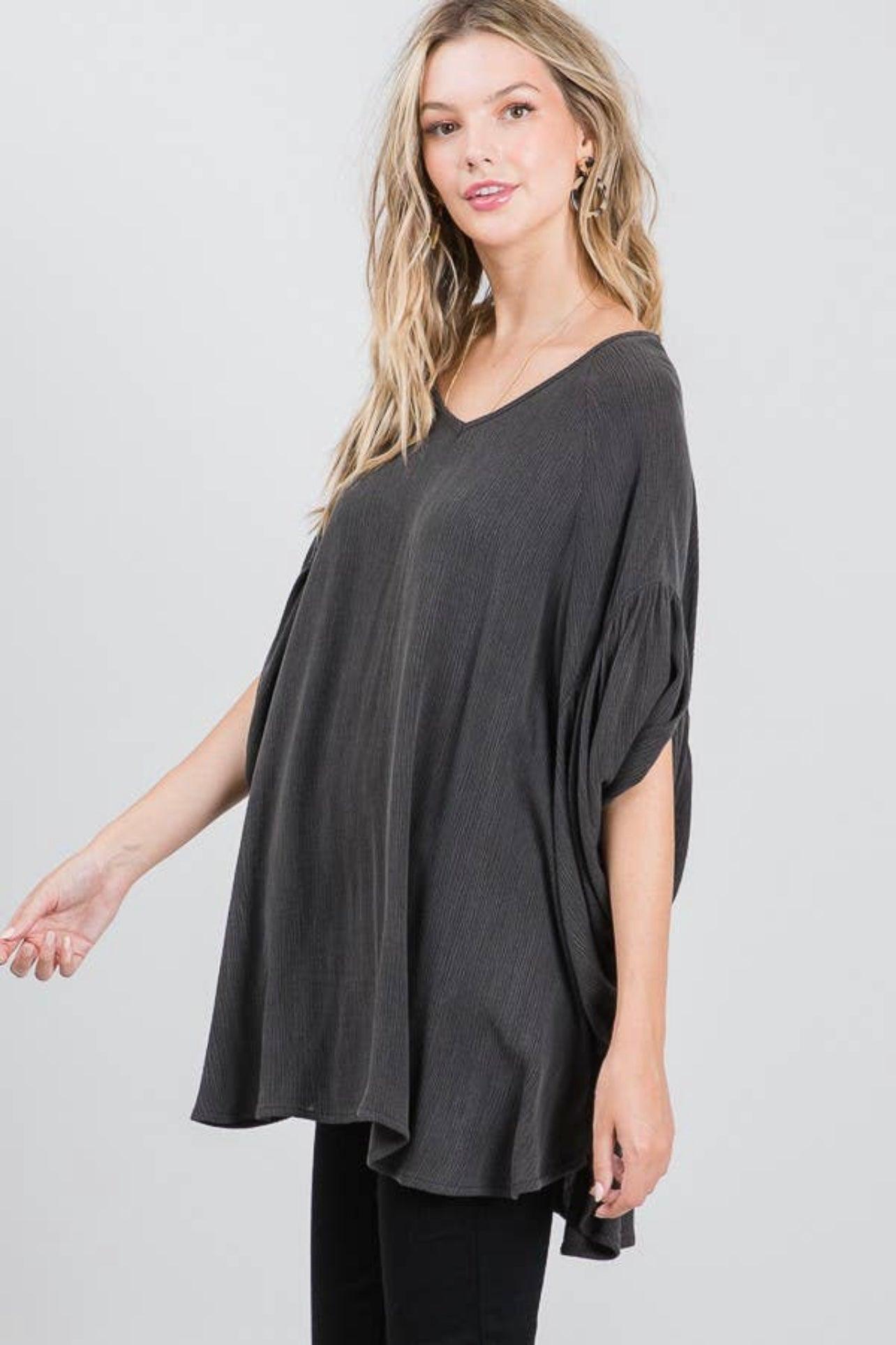 Young woman wearing charcoal textured oversized tunic with gathered short sleeves against neutral background