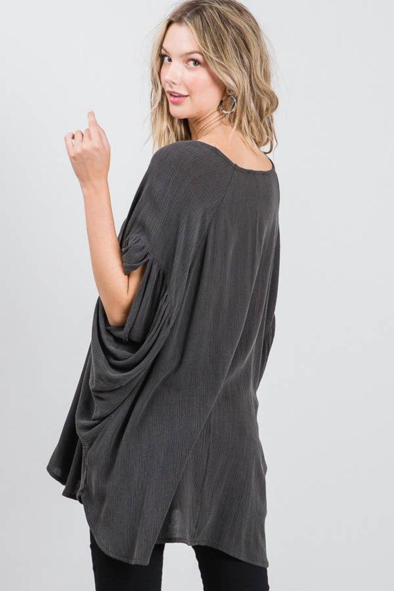 Woman in charcoal loose fit tunic with gathered sleeves looking over shoulder against light gray background