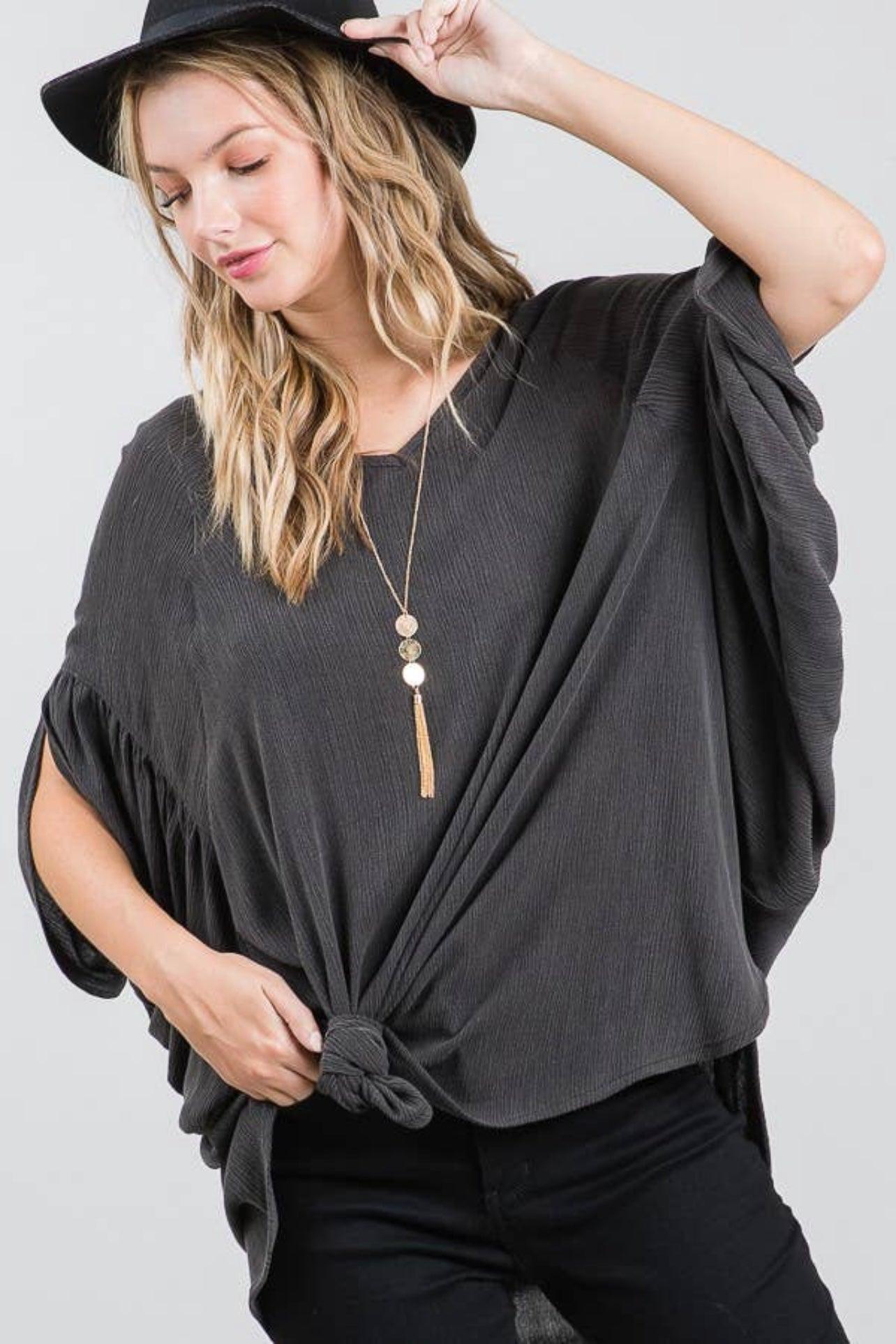 Woman wearing charcoal loose fit textured tunic with knotted front and wide sleeves paired with black pants and black hat