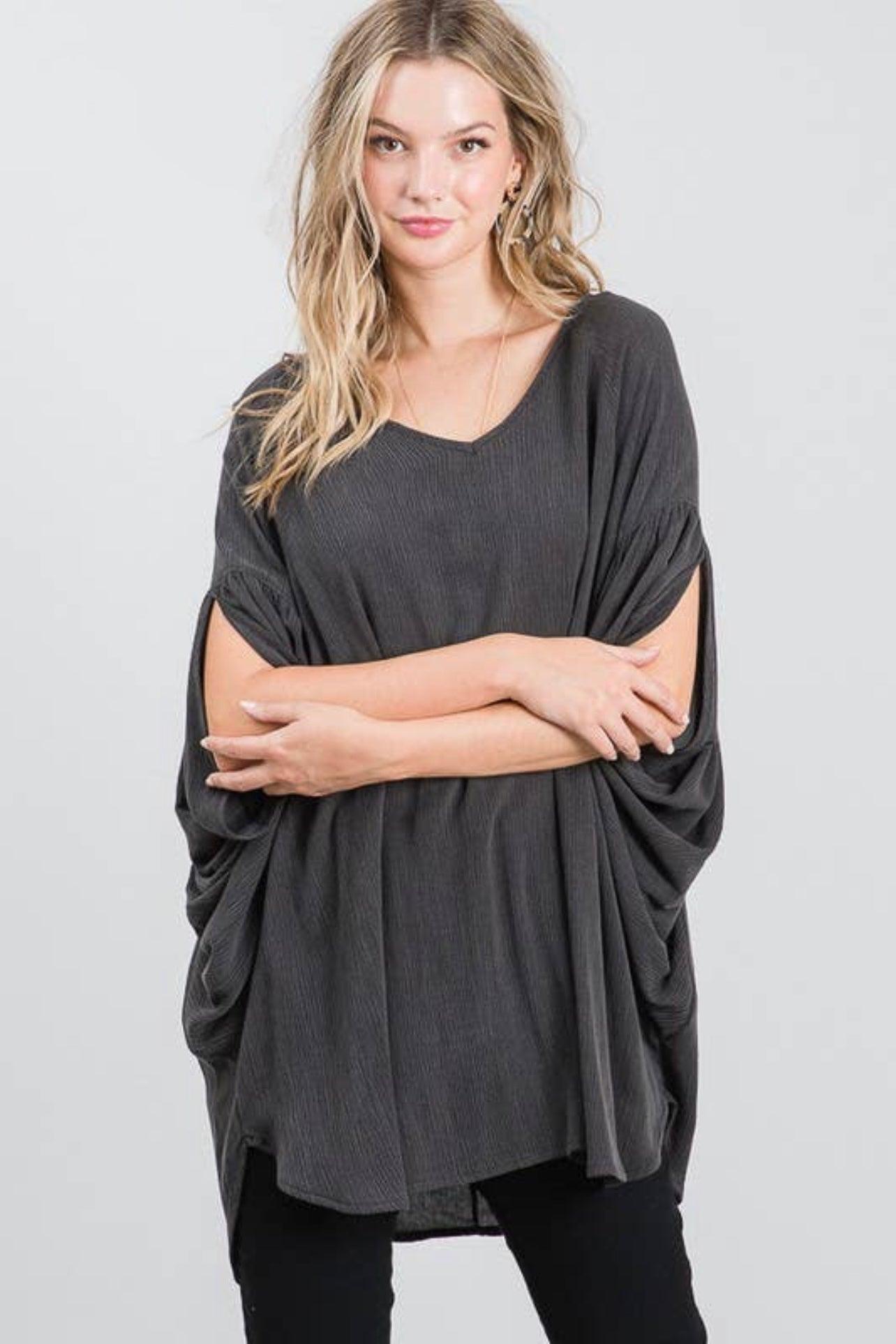 Woman wearing charcoal loose fit tunic with draped sides and v-neck posing with arms crossed against gray background