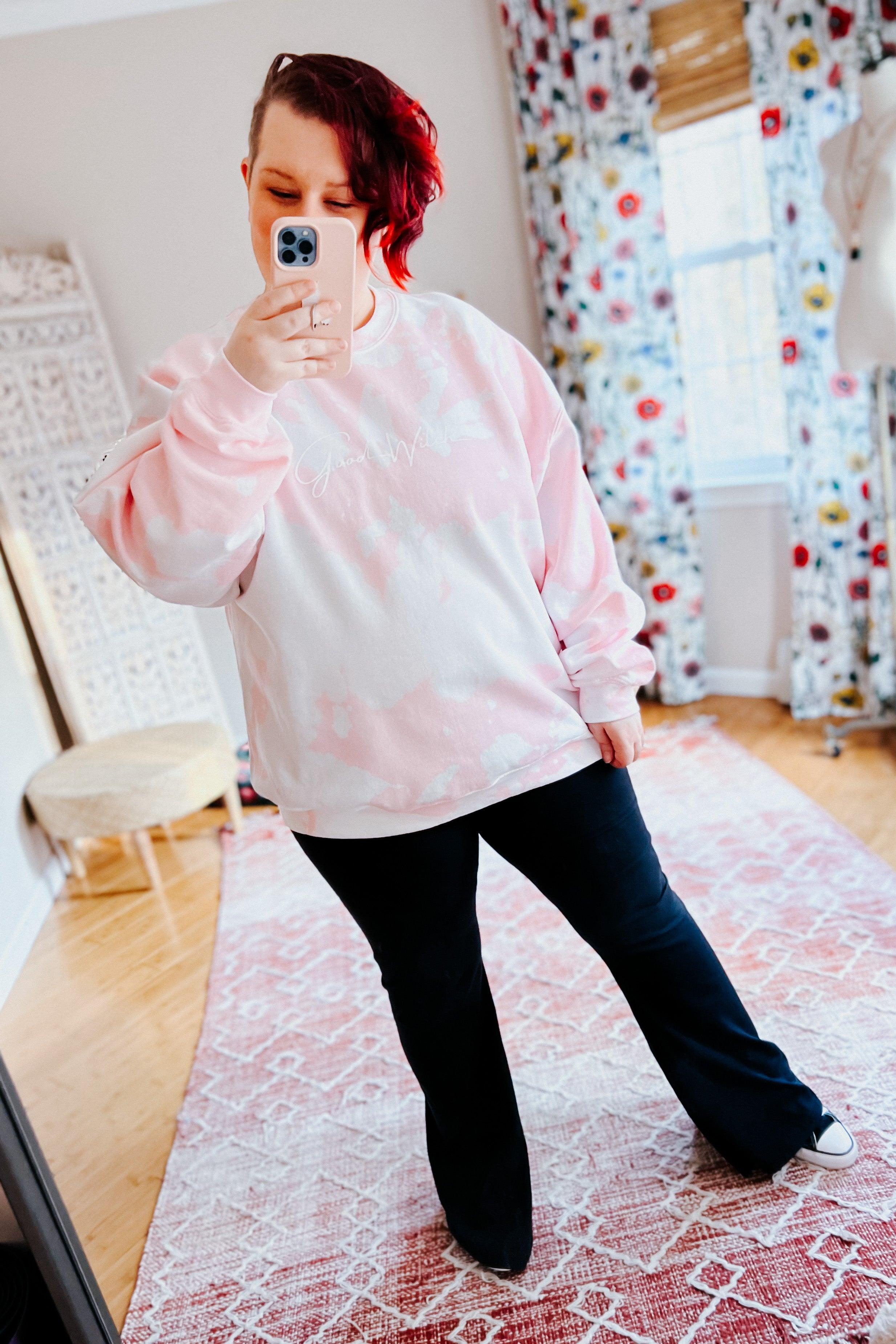 Woman taking mirror selfie wearing a soft pink bleached pullover paired with black flare pants in bright room