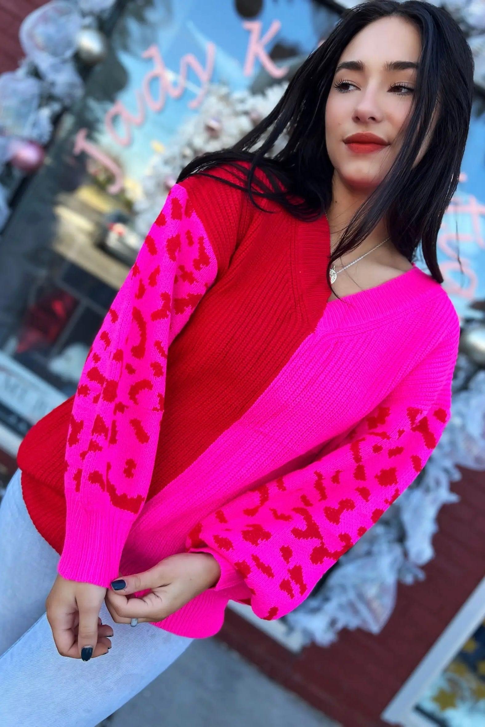 Woman wearing vibrant plush pink and red color block sweater with leopard print sleeves outside shop window