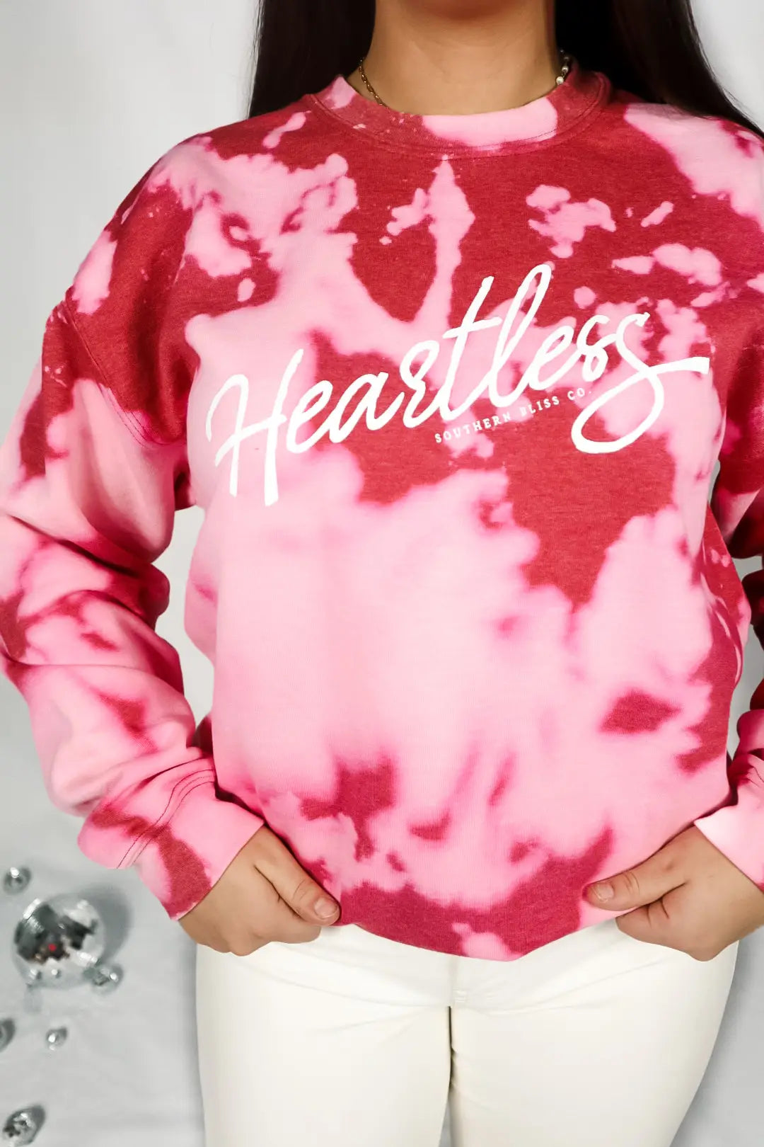 Close-up of woman wearing red heartless bleached pullover with tie-dye pattern and white script logo on front