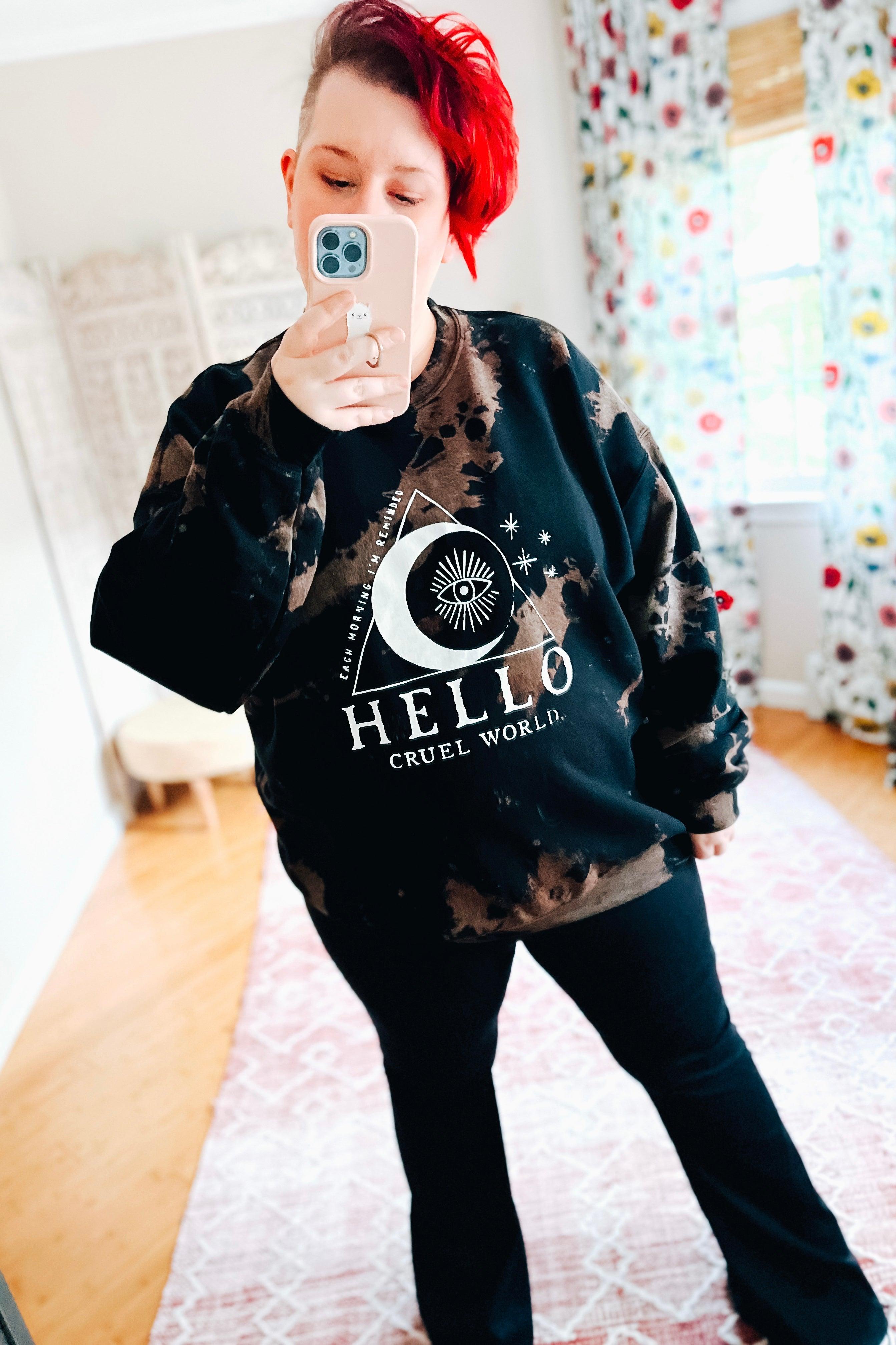 Woman with red hair taking mirror selfie wearing black Hello Cruel World bleached sweatshirt with celestial print indoors