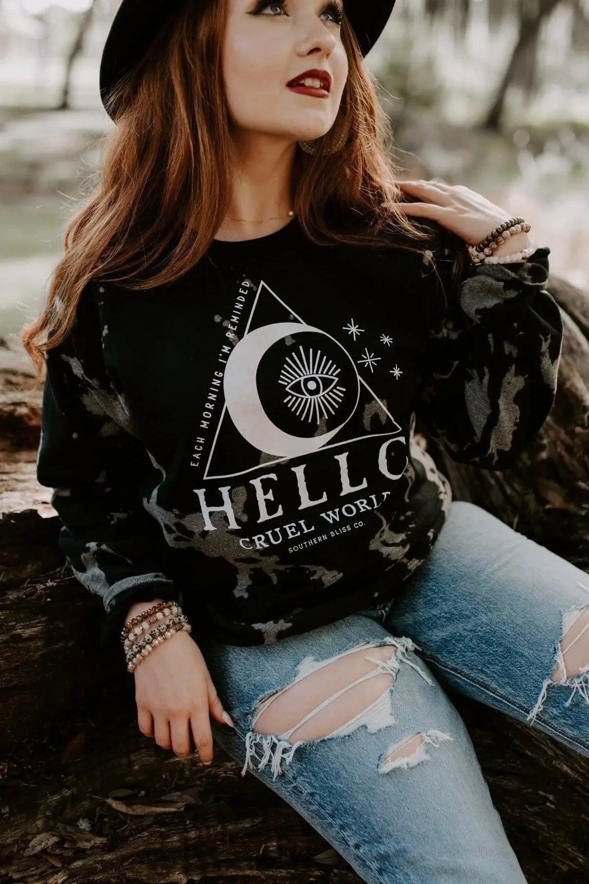 Woman wearing black Hello Cruel World bleached sweatshirt with celestial graphic, paired with ripped light blue jeans outdoors