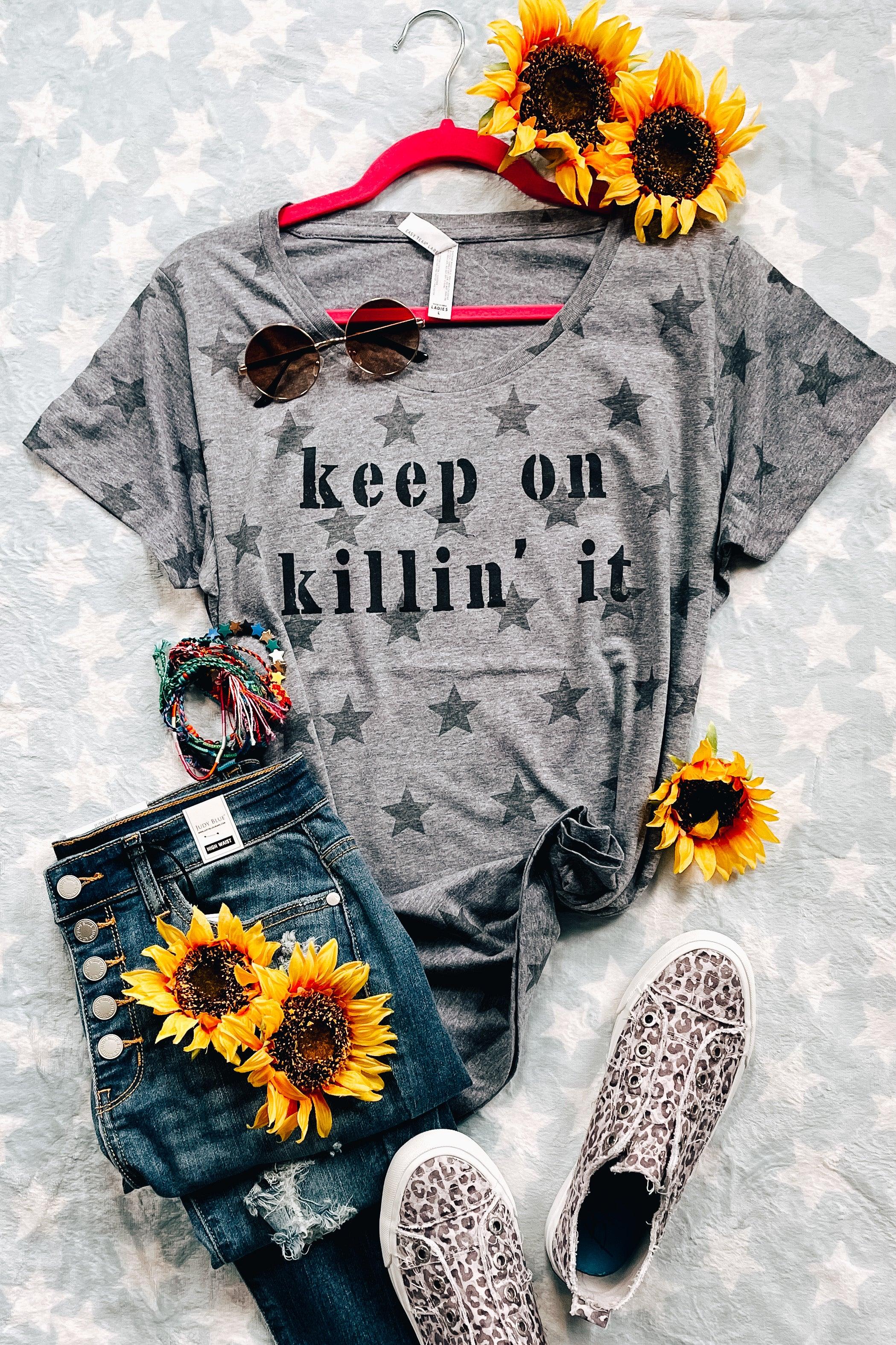 Grey Keep On Killin’ It Star Tee with black star pattern displayed with distressed button-fly jeans, leopard print shoes, and sunflowers