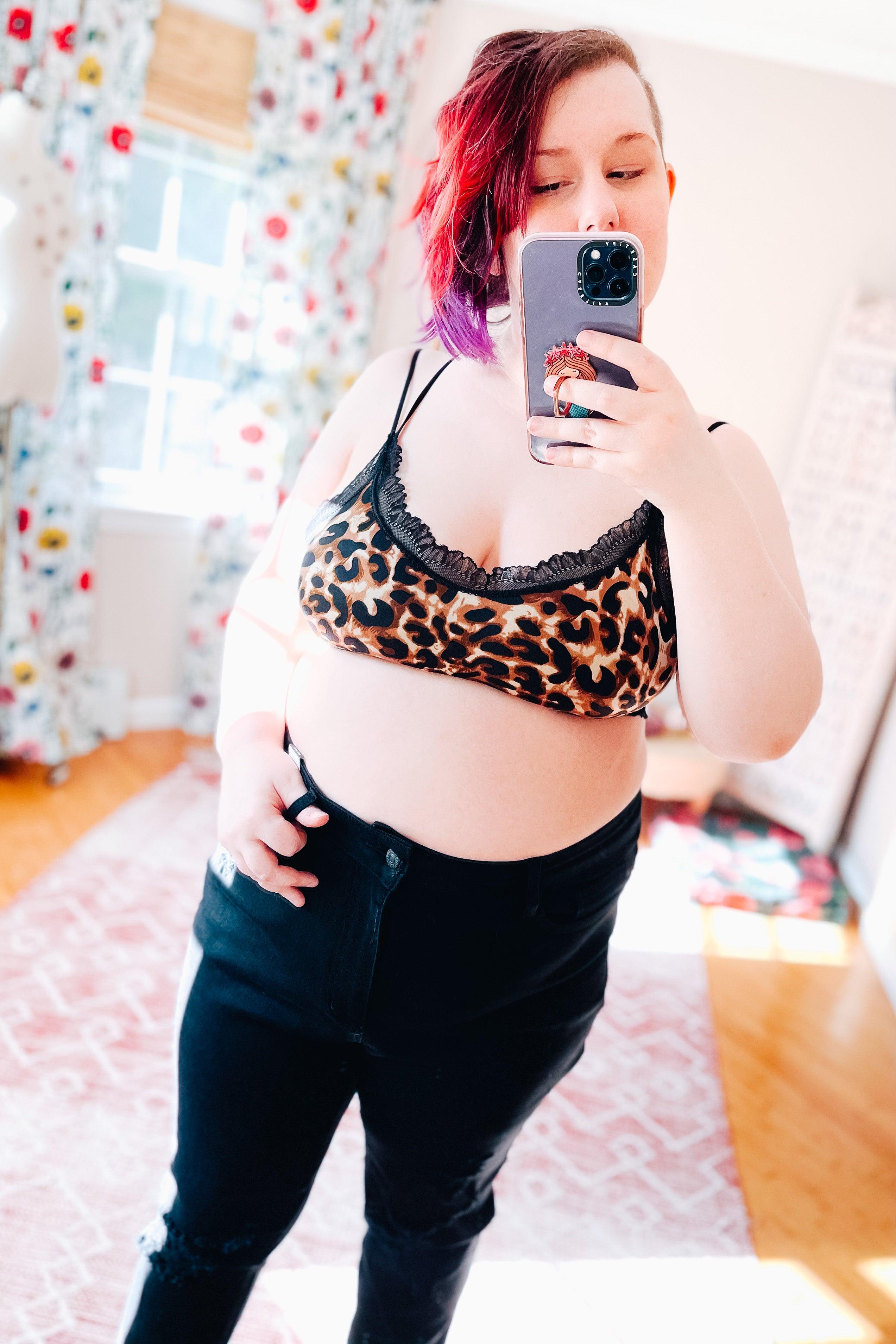 Woman taking a mirror selfie wearing a brown and black animal print bralette with black lace trim and black pants indoors