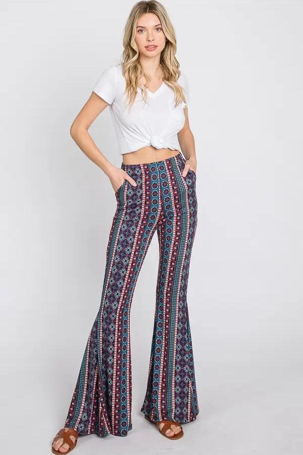 Woman wearing high-waisted blue patterned flare pants with hands in pockets and a white knotted cropped top