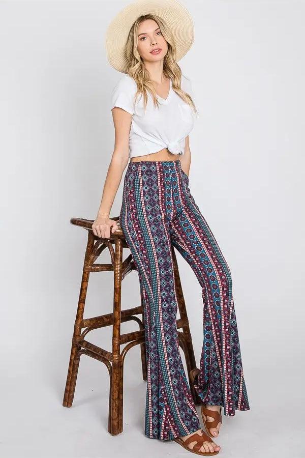 Woman wearing high-waisted blue patterned flare pants with a knotted white cropped t-shirt and straw hat