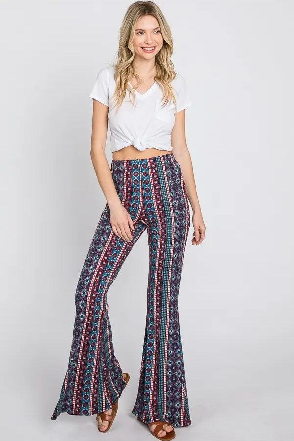 Woman wearing blue patterned bohemian style flared pants with a knotted white short sleeve top and sandals
