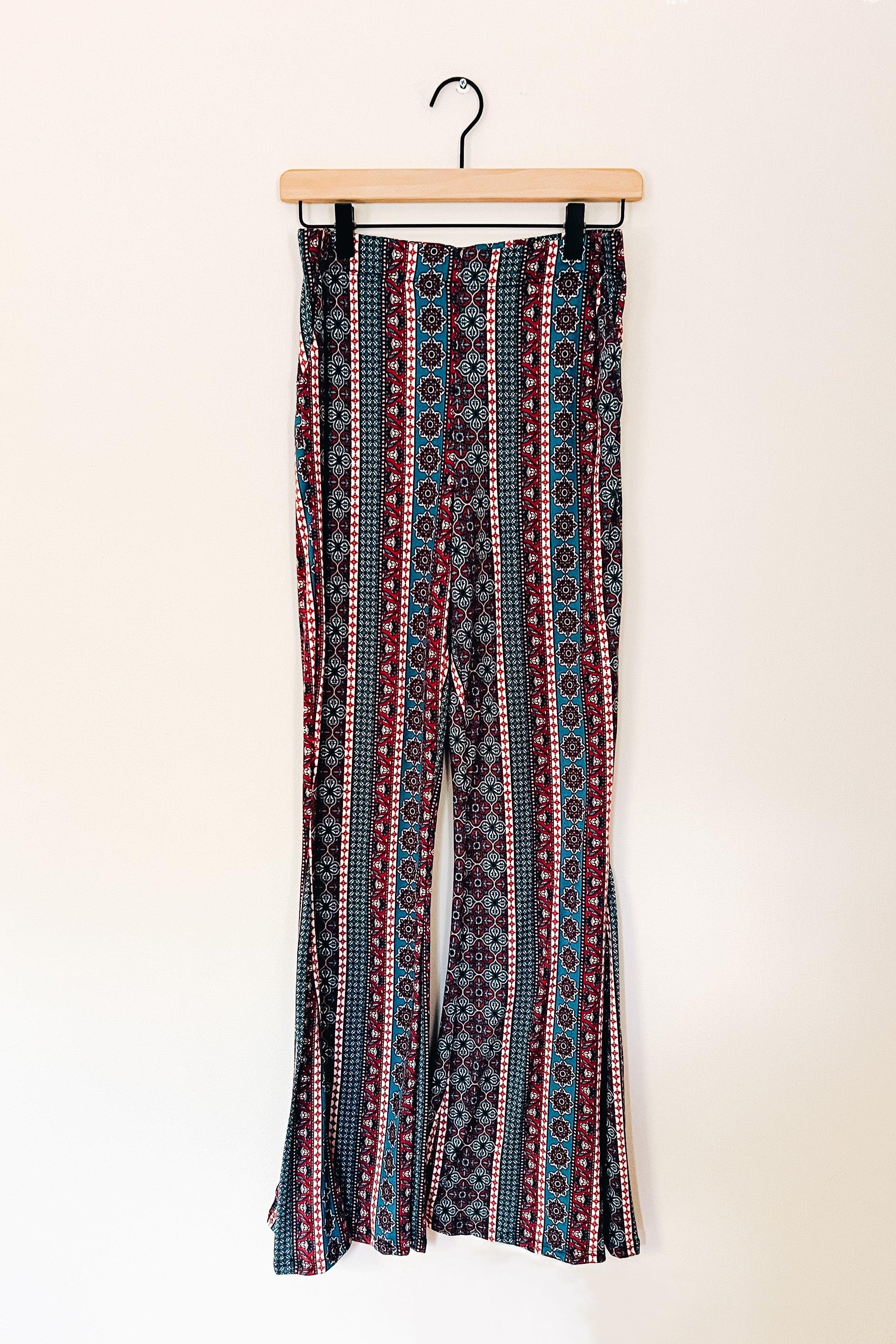 Bohemian style pants with vertical stripes and geometric patterns in blue, red, black, and white hanging on a wooden hanger