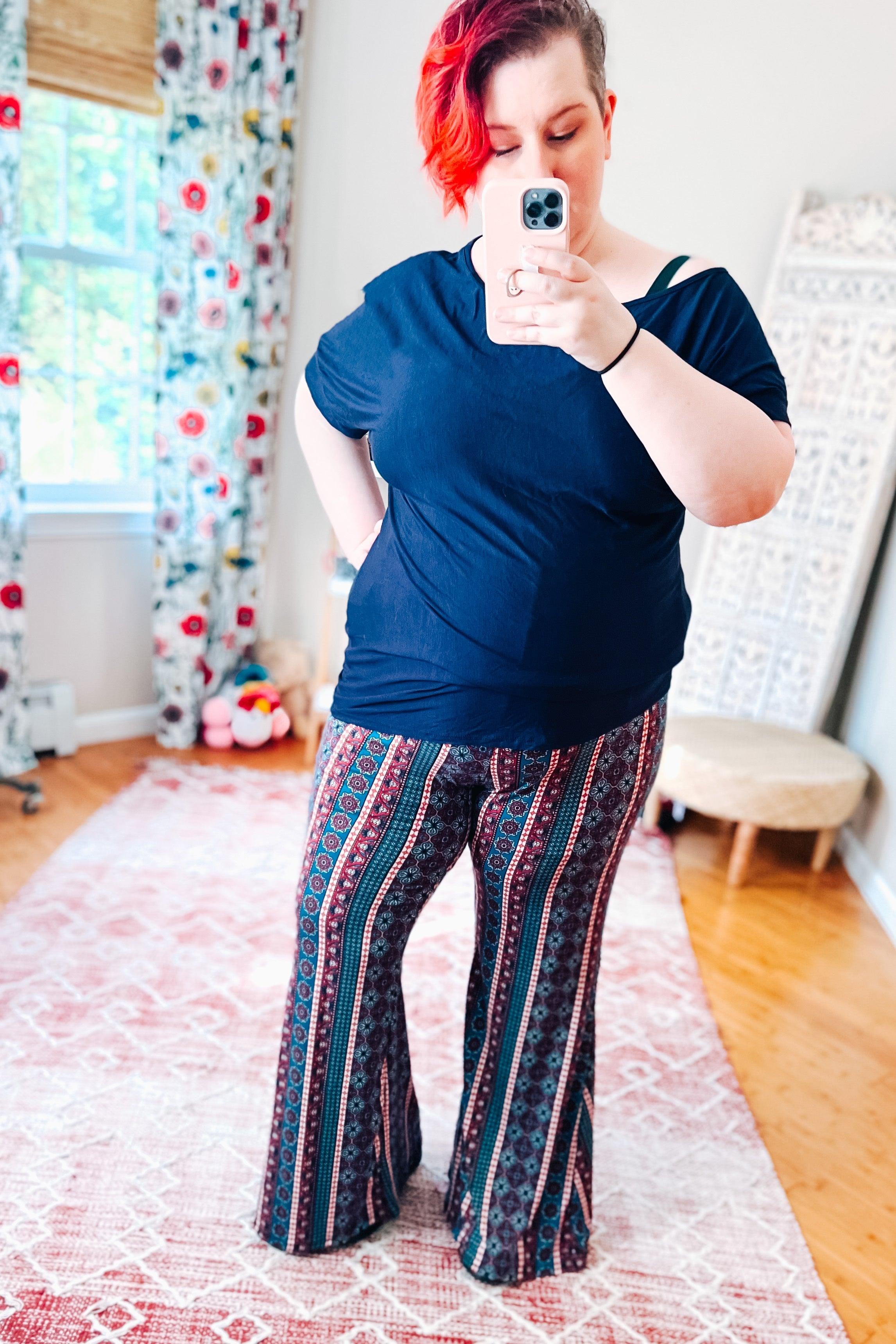 Woman wearing patterned flare pants with vertical stripes in blue and red tones paired with a loose dark blue top indoors