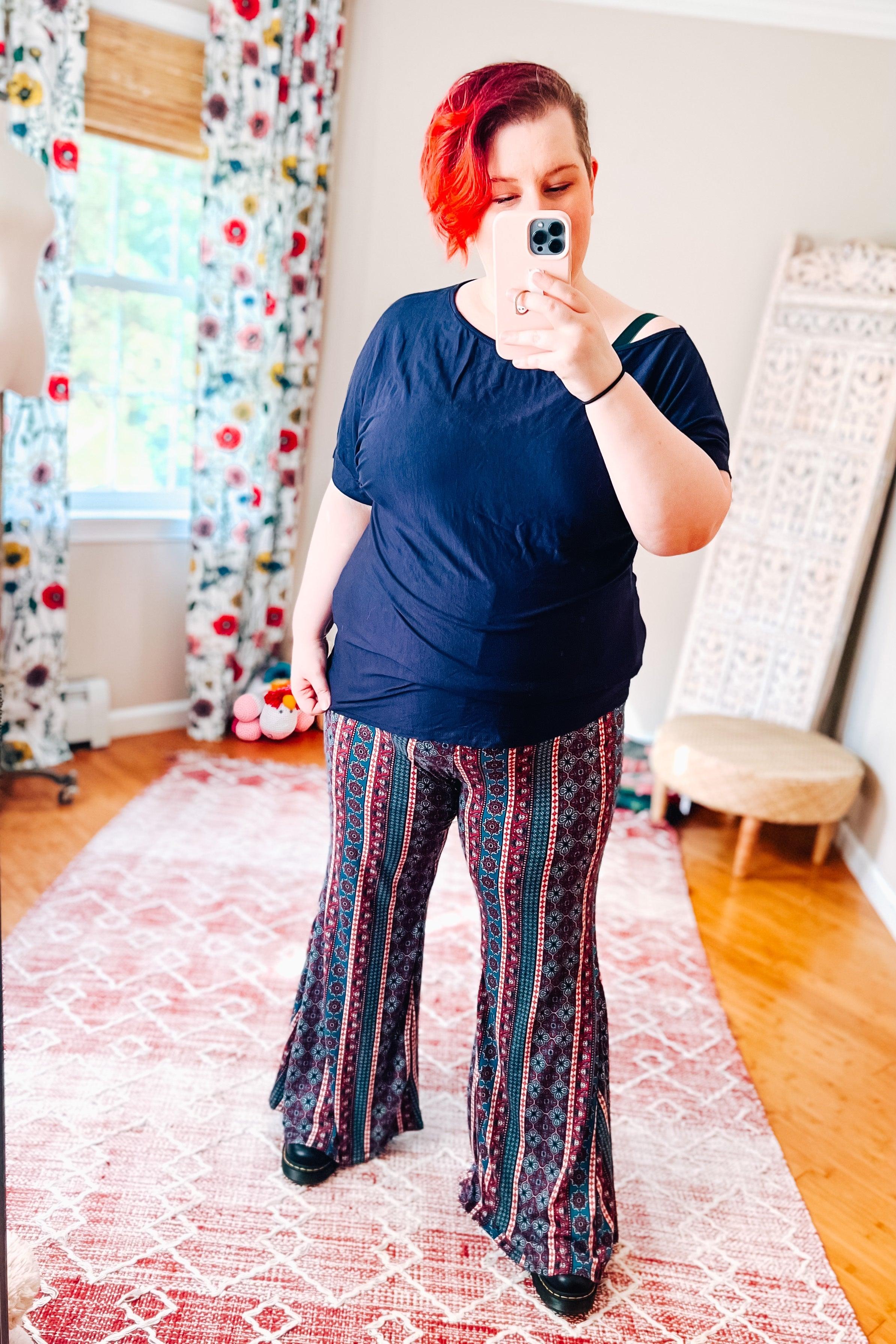 Woman wearing boho style flared pants with vertical red and blue patterns paired with a navy blue short sleeve top indoors
