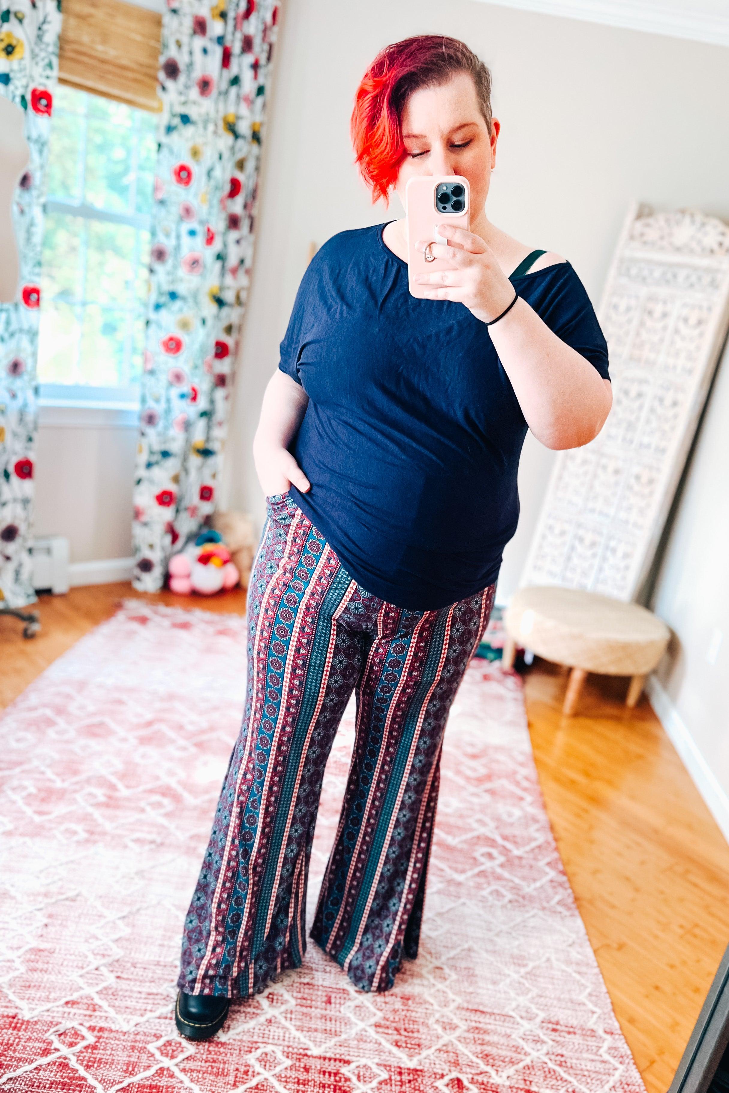 Woman wearing patterned flare pants with vertical stripes in red, blue, and black paired with a loose black top indoors