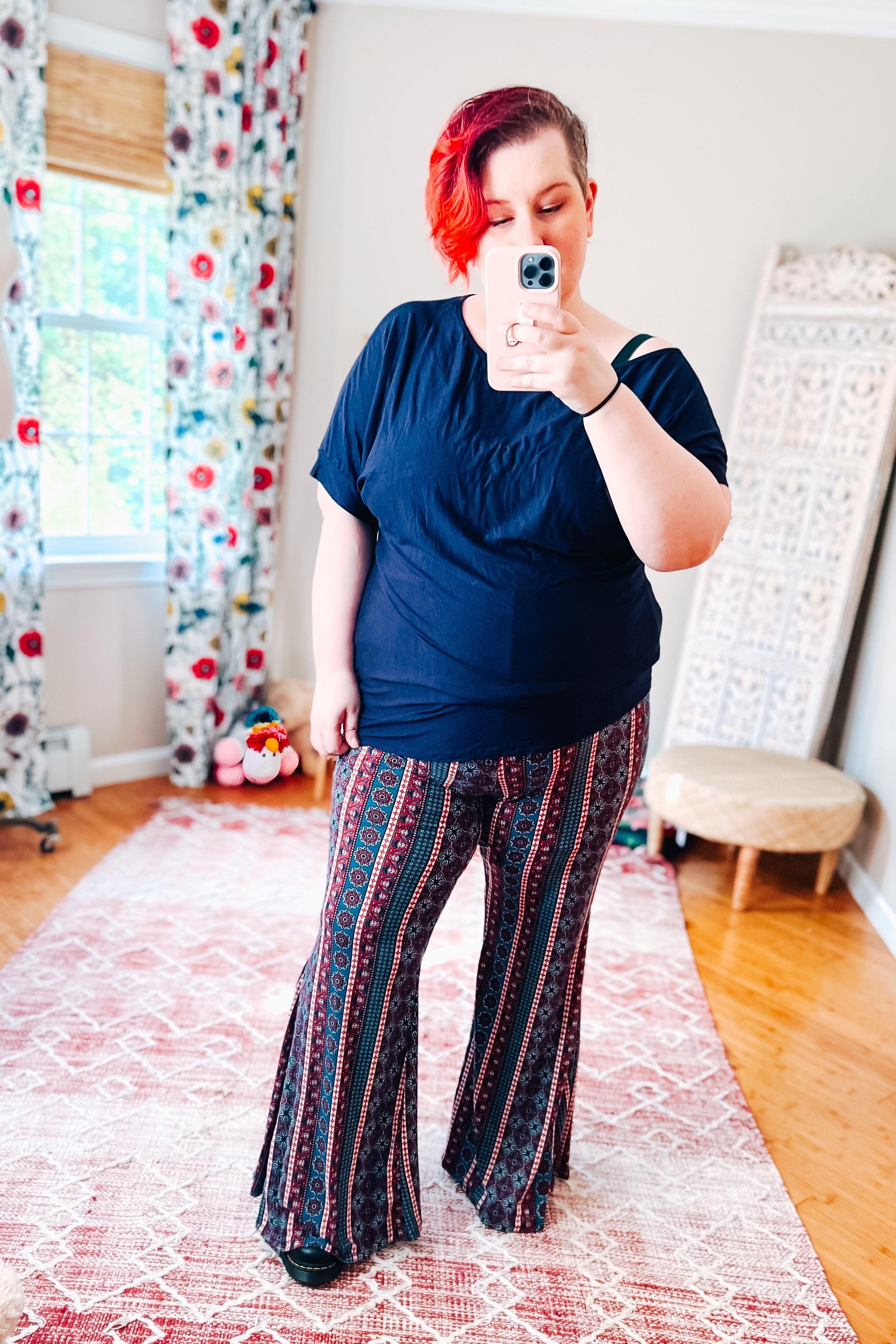 Woman wearing patterned boho flare pants with vertical geometric designs in blue and red paired with a loose dark navy top indoors