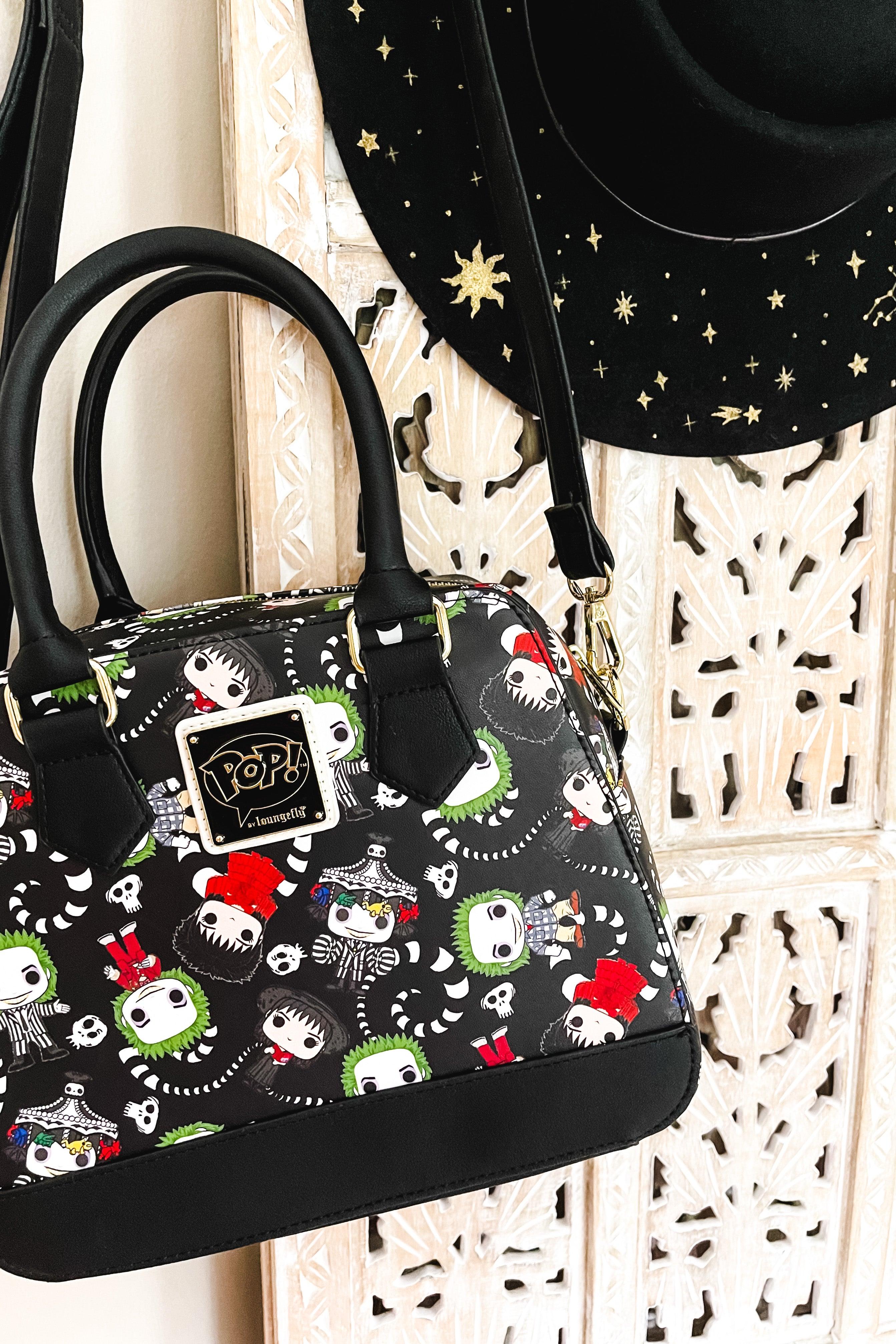 Black loungefly handbag with colorful pop-style beetlejuice characters and skeleton designs hanging beside a black velvet hat with gold celestial embroidery