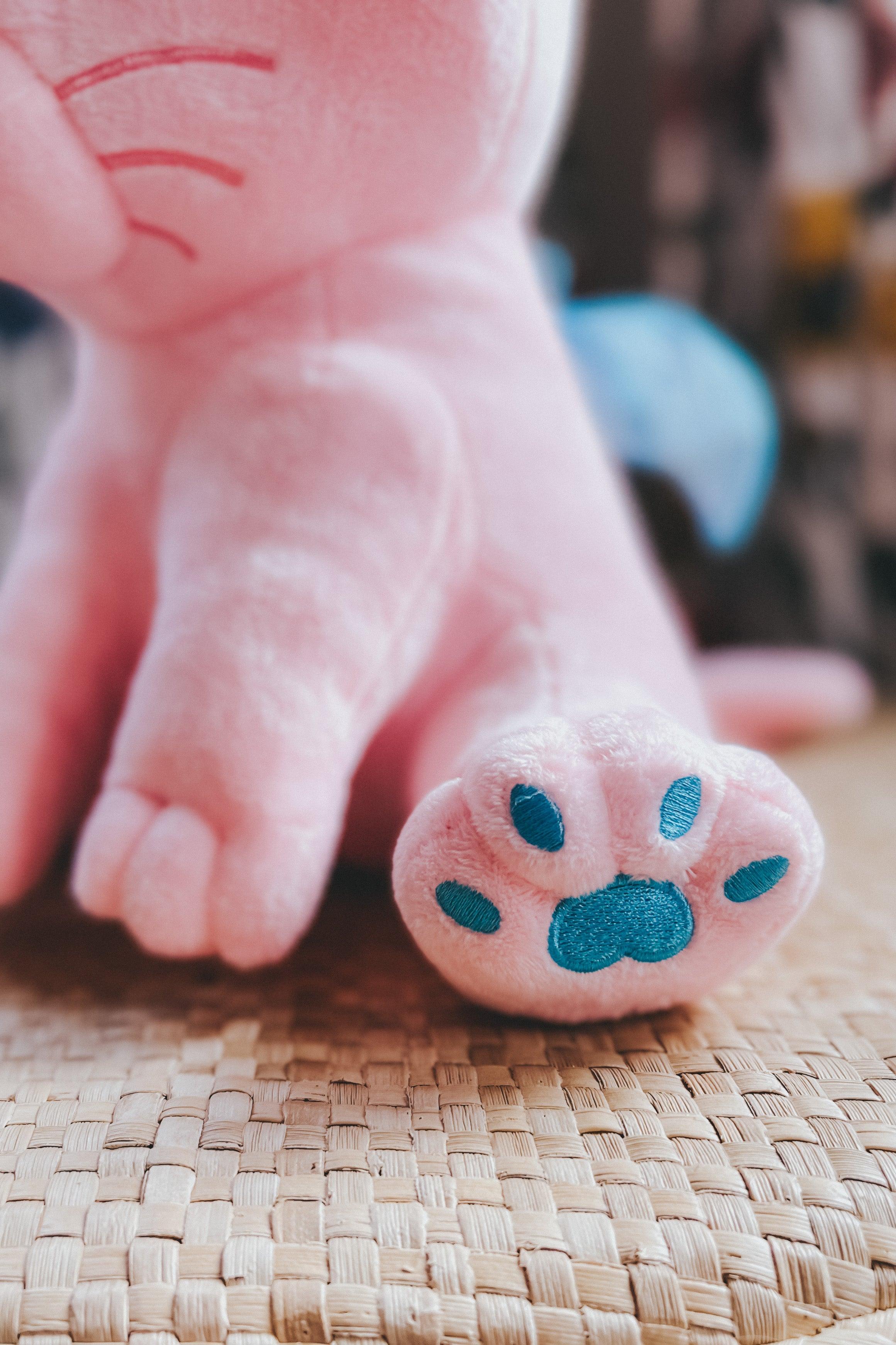 Close-up of plush cotton candy pink paw with blue embroidered pads on woven mat background