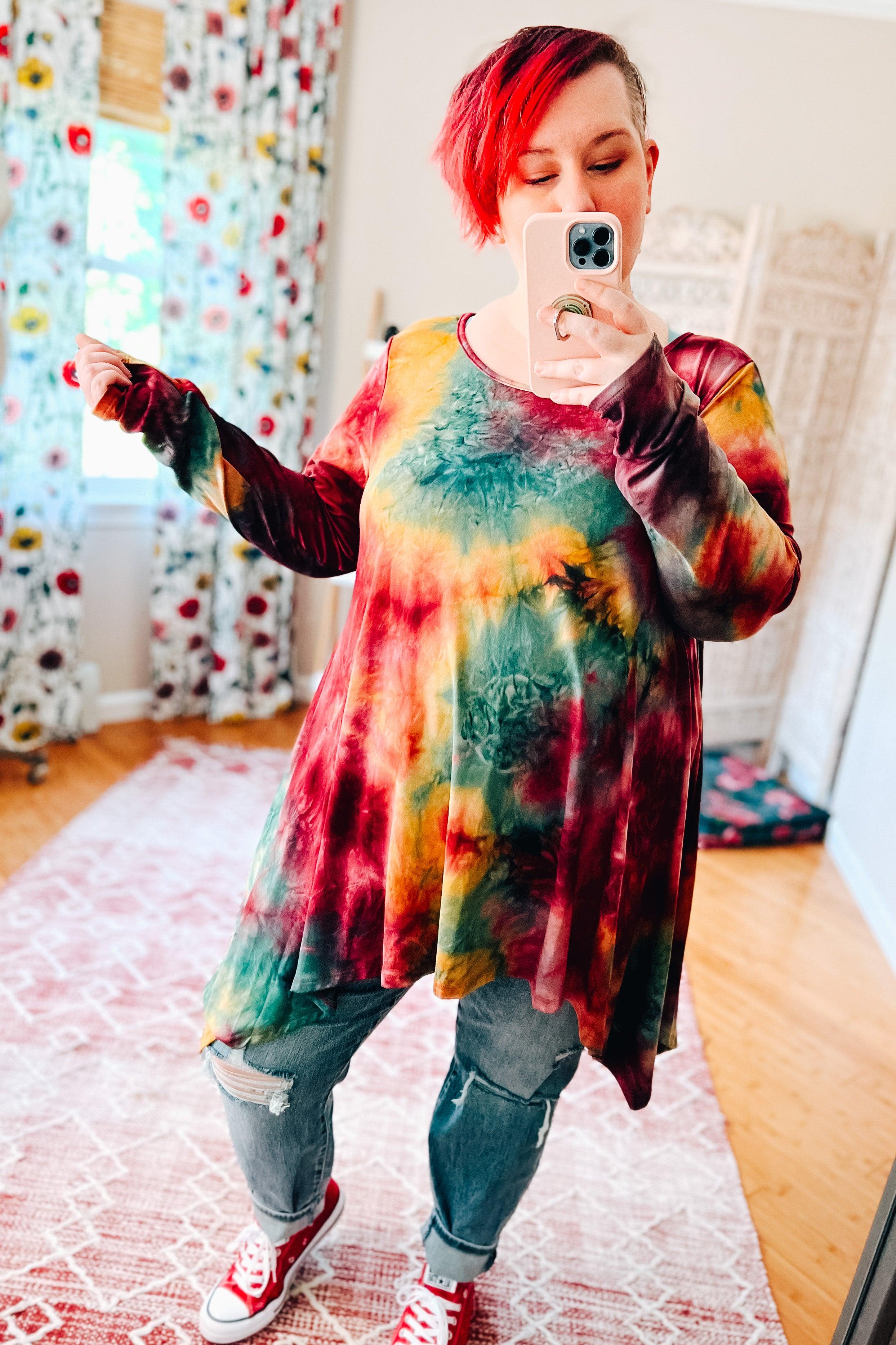 Vibrant long-sleeve tie-dye top with ruby, green, and mustard hues paired with ripped jeans and red sneakers
