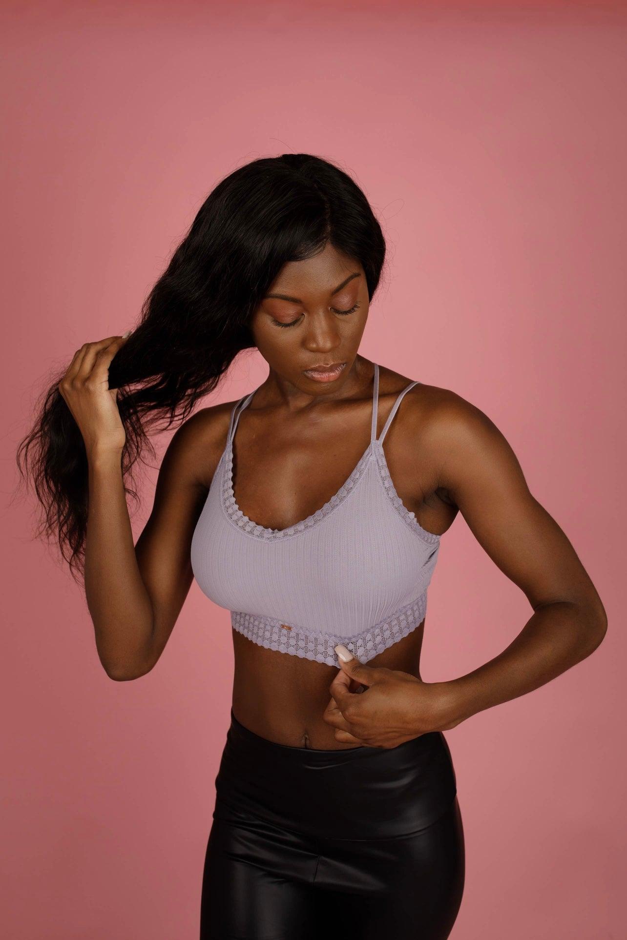Woman adjusting her long hair wearing a lilac ribbed bralette with lace trim and thin straps against pink background