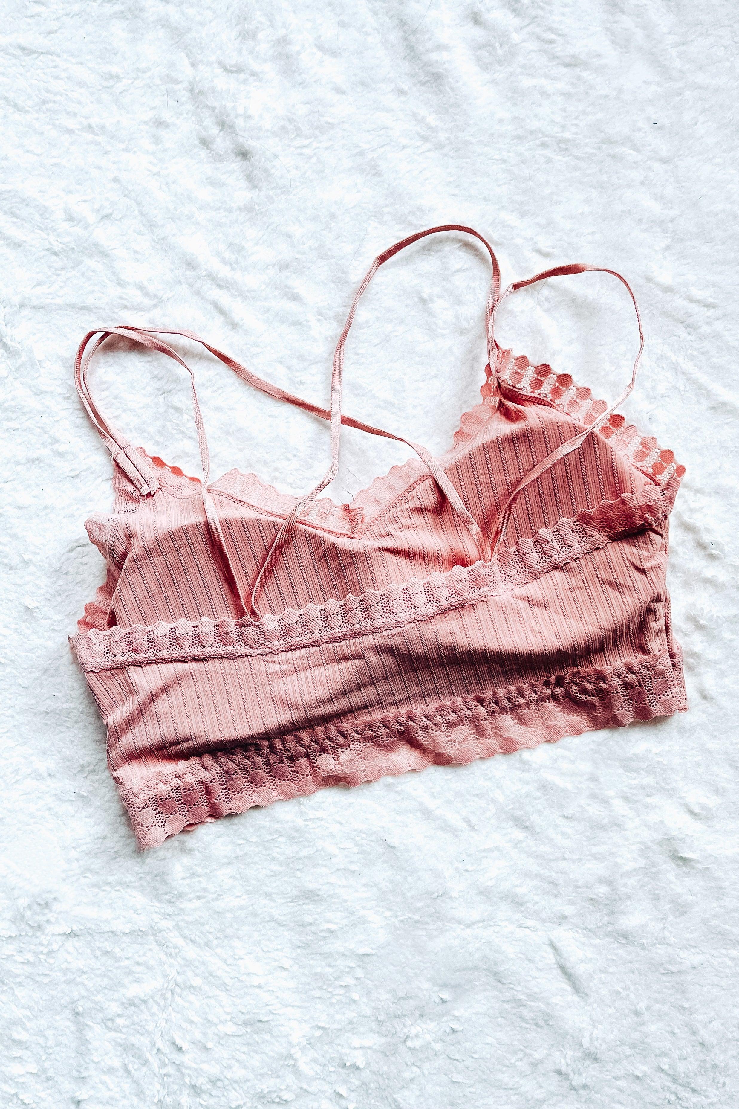 Pink lace bralette with ribbed detail and scalloped lace trim, laid flat on soft white fabric background