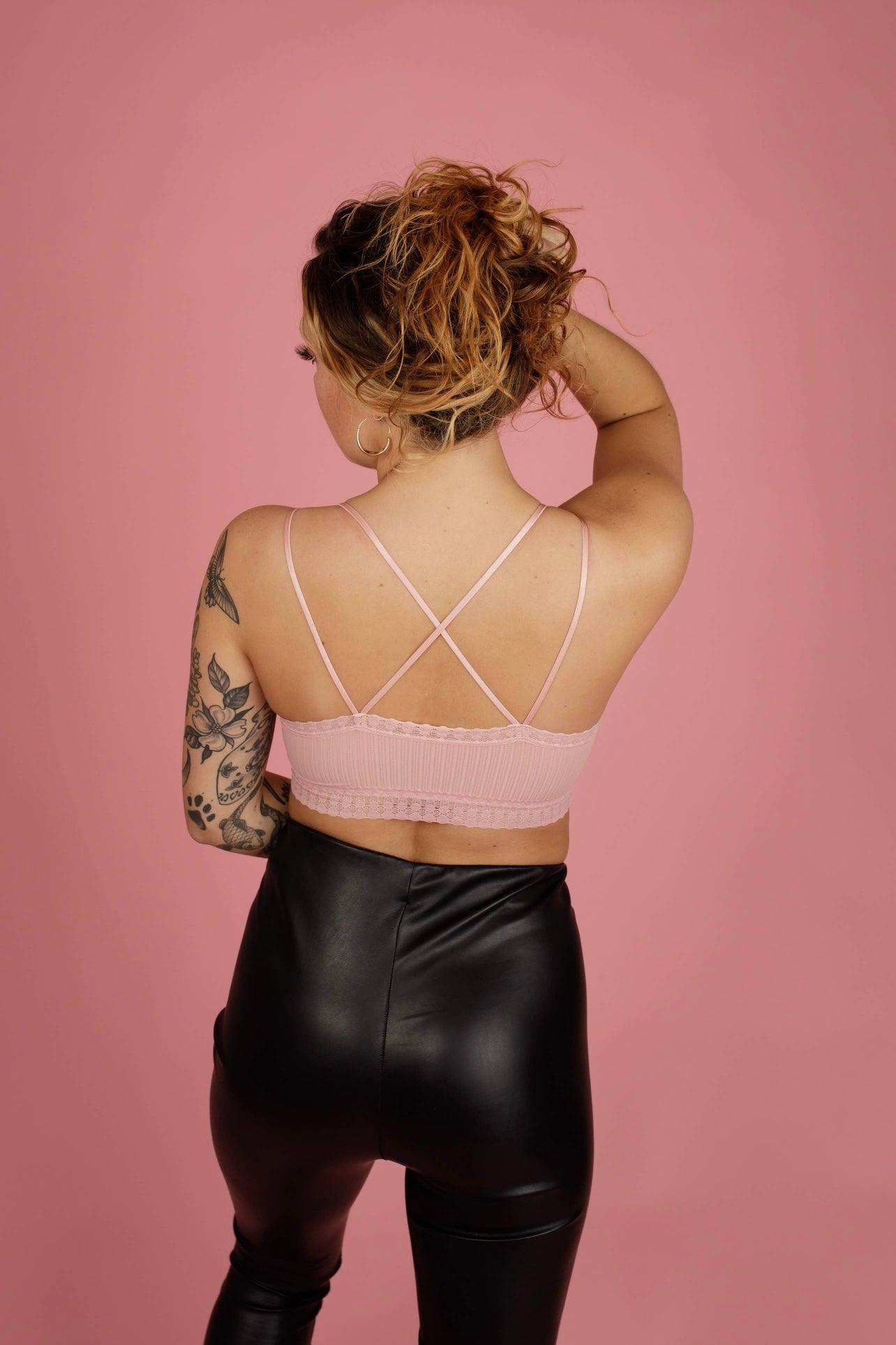 Woman with tattoos styling curly hair wearing soft pink lace bralette with crisscross straps and black leather pants