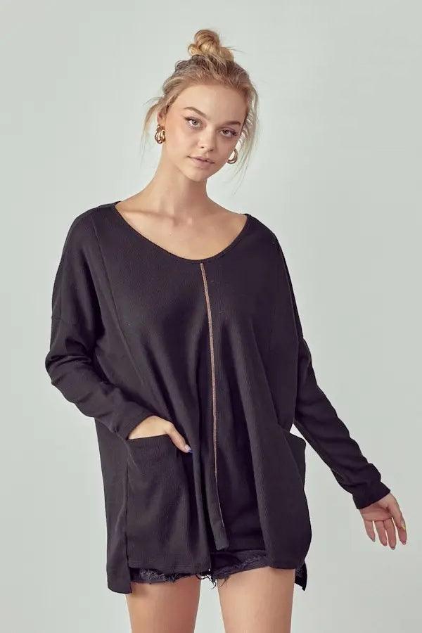 Woman wearing a relaxed black oversized thermal tunic with front pockets and a subtle center seam detail