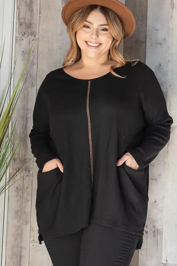 Smiling plus-size woman wearing a black oversized thermal tunic with front seam and pockets and a brown hat indoors