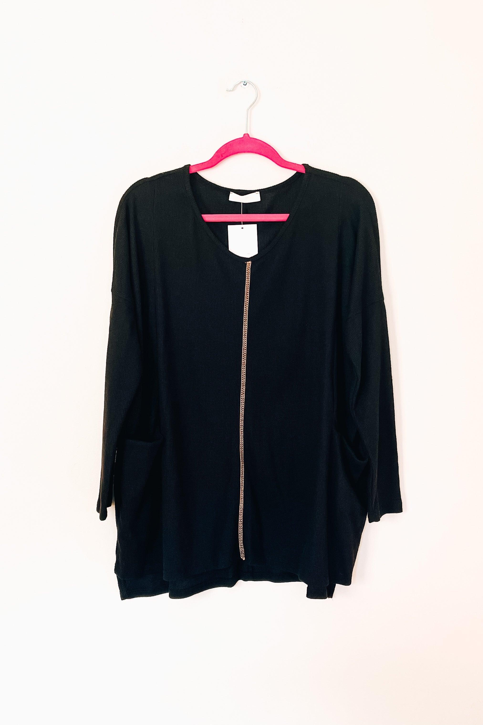 Black oversized thermal tunic with front seam detail and pockets hanging on bright pink hanger against white background