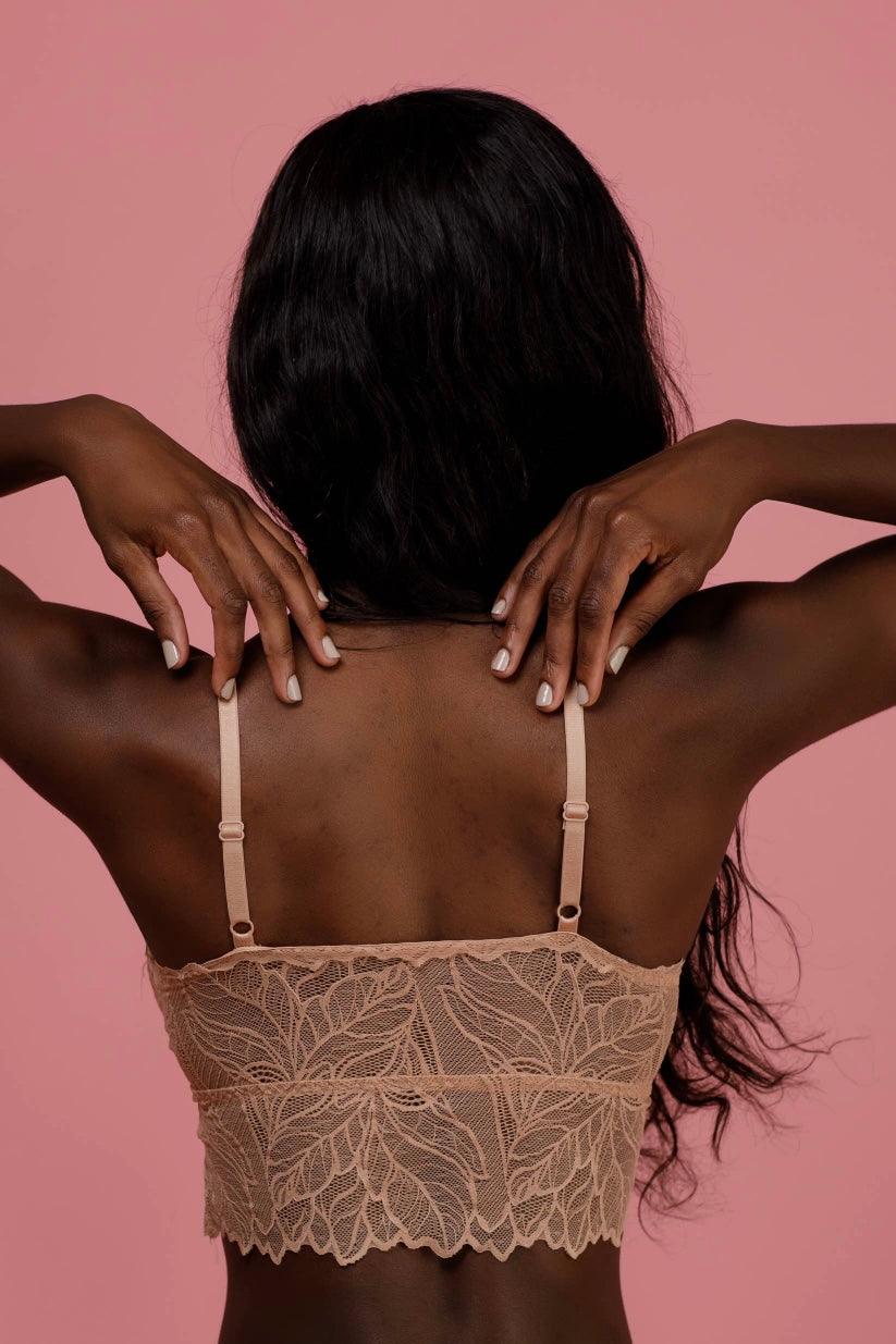 Back view of a brick-colored lace bralette with adjustable straps and intricate floral lace patterns worn by a model against a muted pink background.