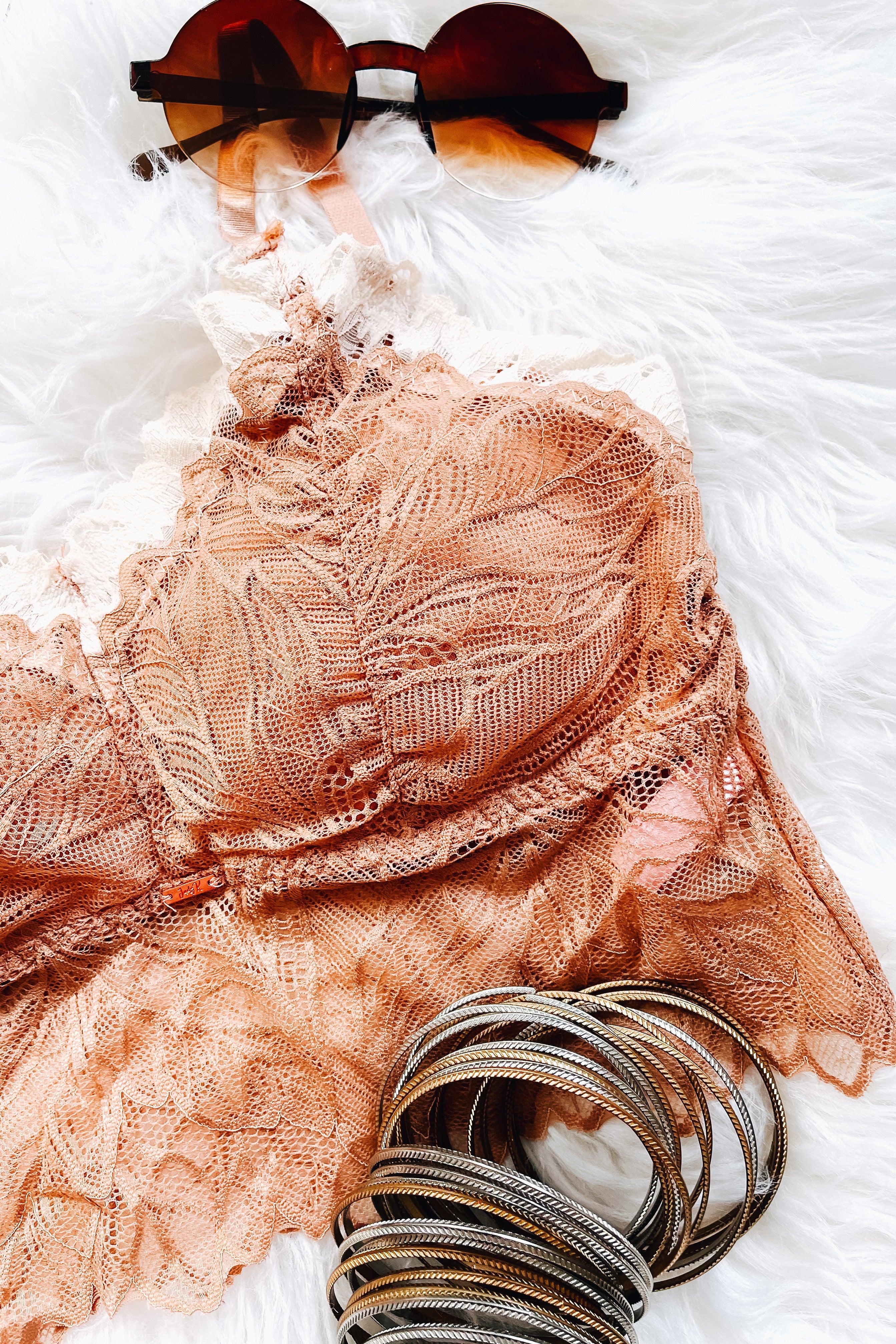 Soft brick-colored lace bralette with delicate leaf lace patterns, styled with round amber sunglasses and stacked metallic bangles on a white fur surface.
