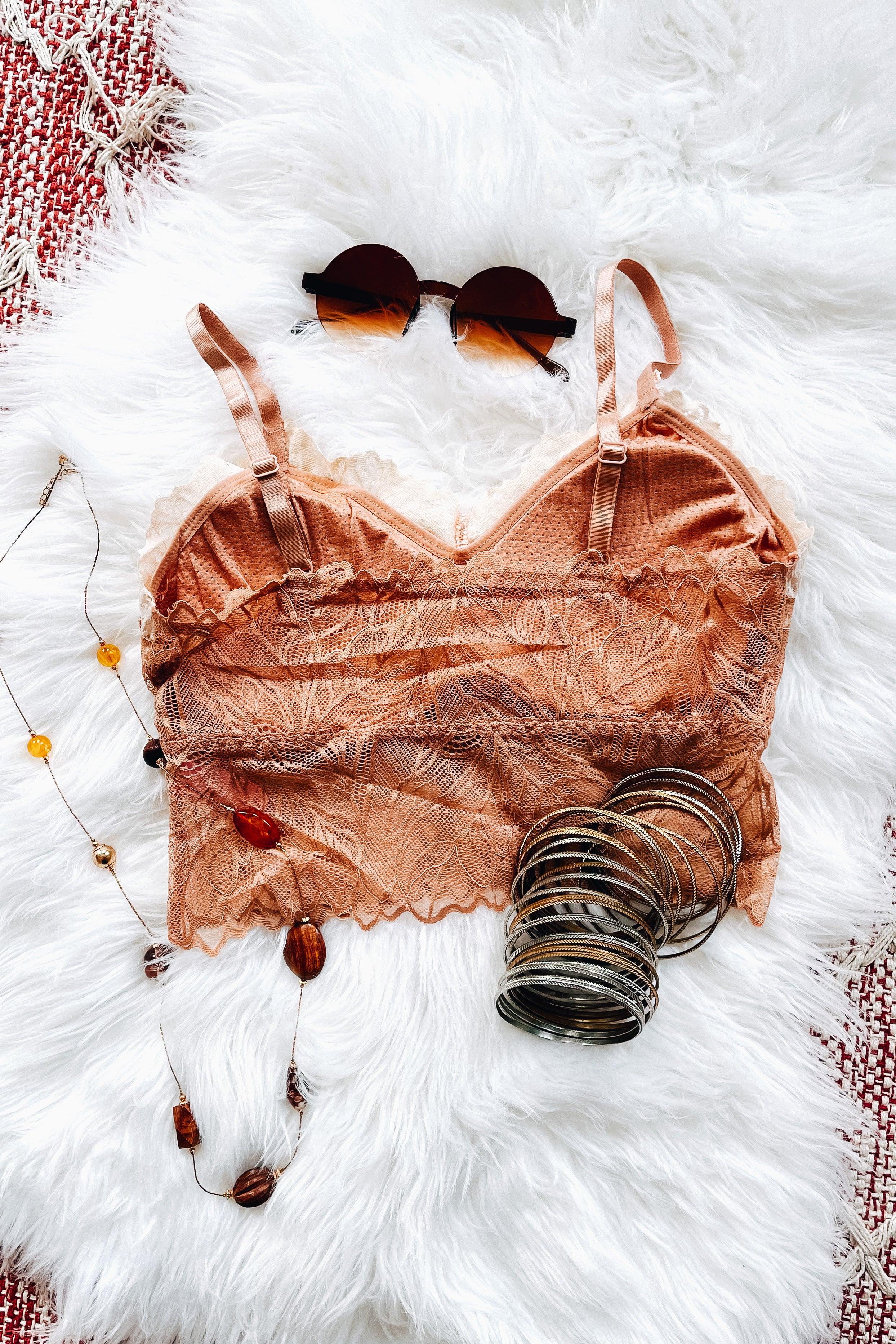Brick-colored lace bralette featuring adjustable straps, styled with round sunglasses, layered amber necklace, and stacked metallic bangles on a white textured surface.