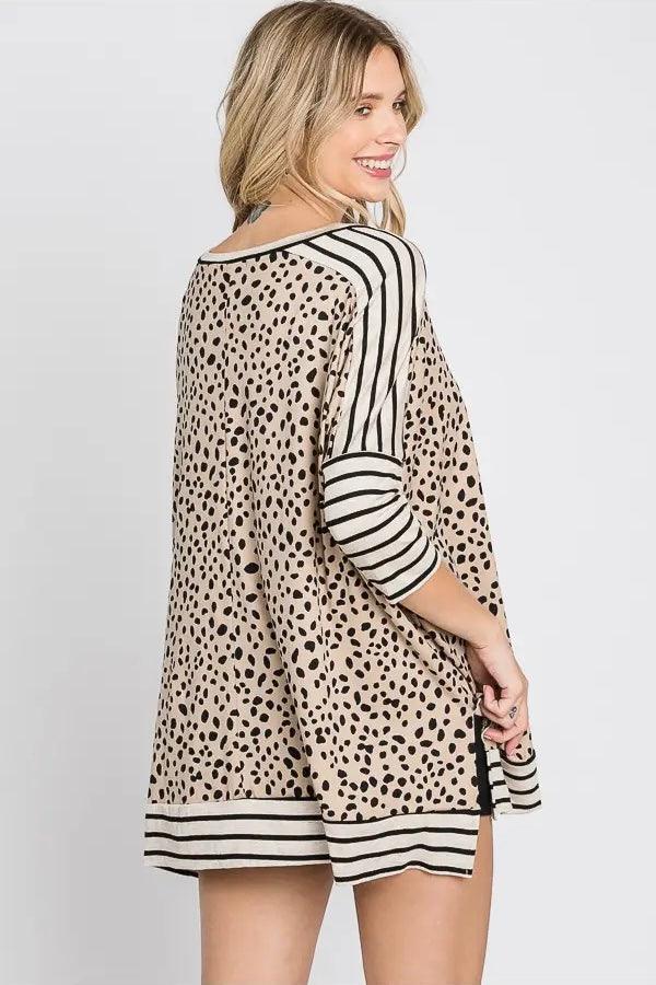 Woman wearing a taupe tunic with black spotted print and contrasting black and white striped sleeves and hem, smiling over her shoulder