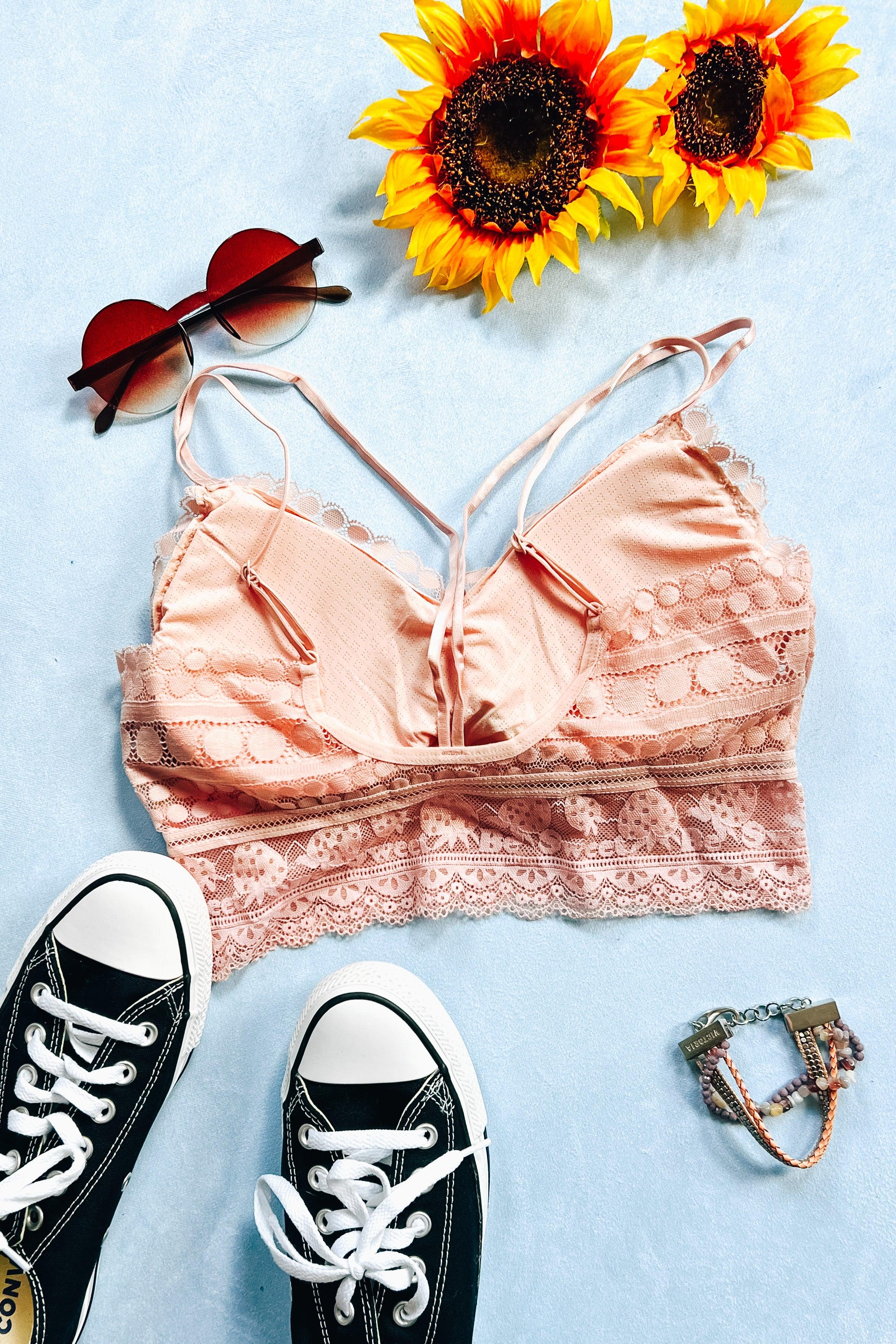 Blush lace bralette with circular and floral patterns styled with heart-shaped sunglasses, black high-top sneakers, beaded bracelet, and sunflowers on light blue background
