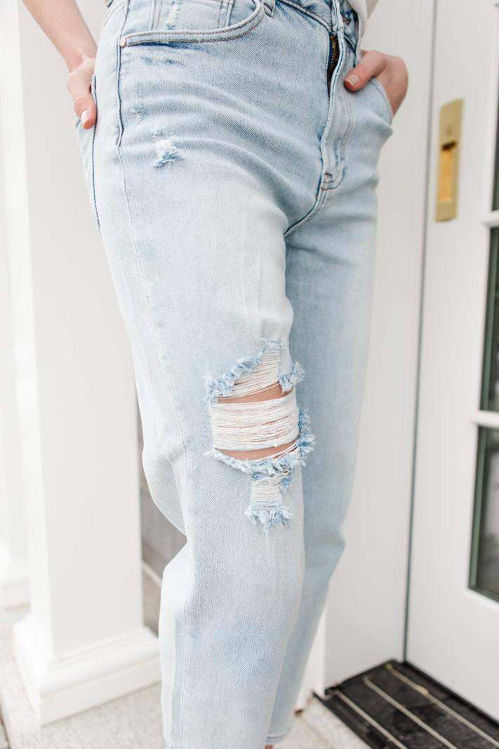 Light blue distressed jeans featuring a large frayed rip on the thigh and a smaller tear near the pocket, worn indoors by a doorway.