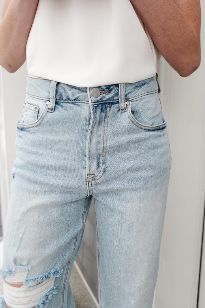 Close-up of light blue jeans with distressed details on the thigh and a high-rise waist, paired with a white sleeveless top
