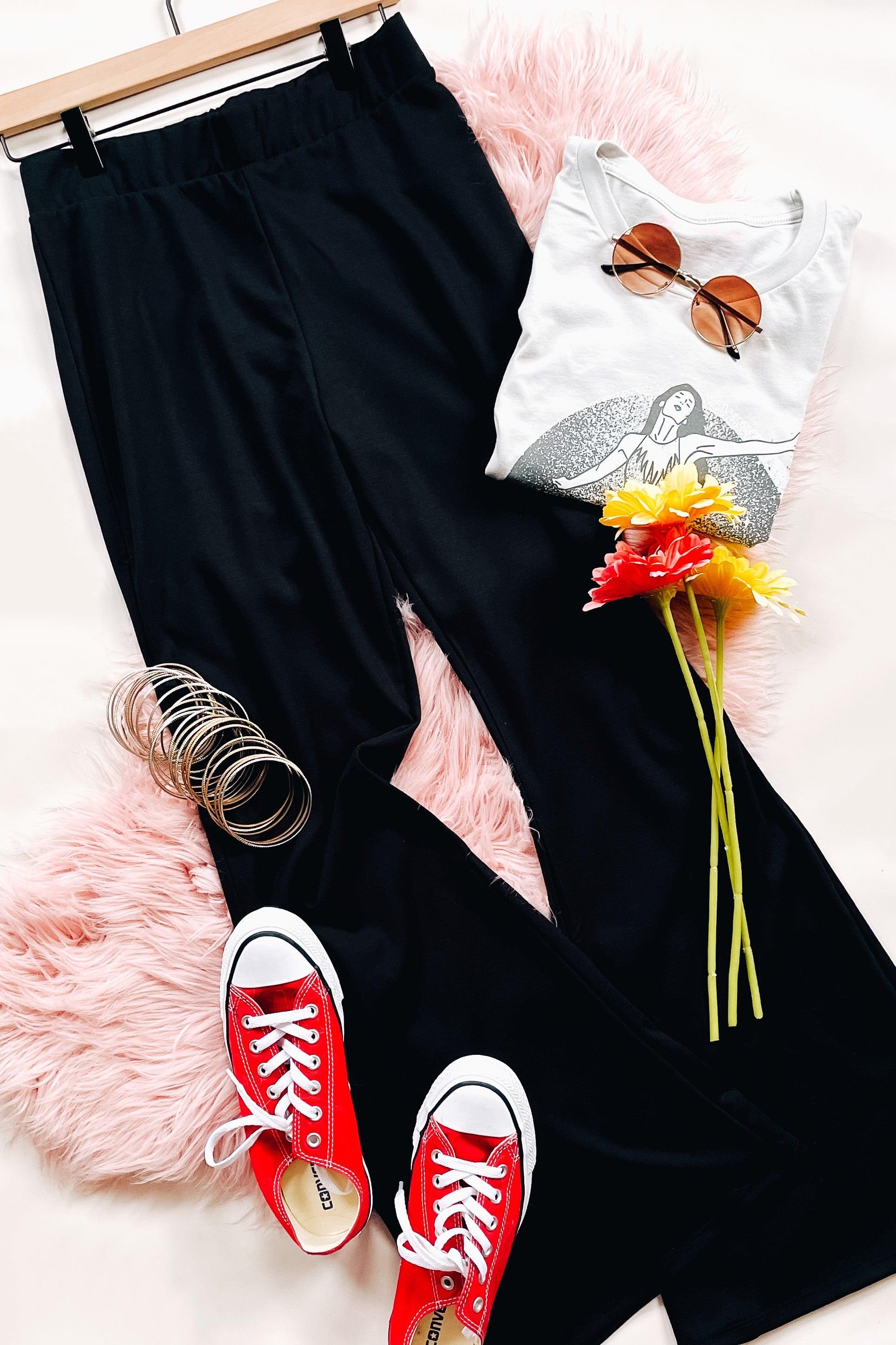 Black flared pants styled with white graphic tee, red canvas shoes, round sunglasses, bracelets, and bright flowers on pink fur
