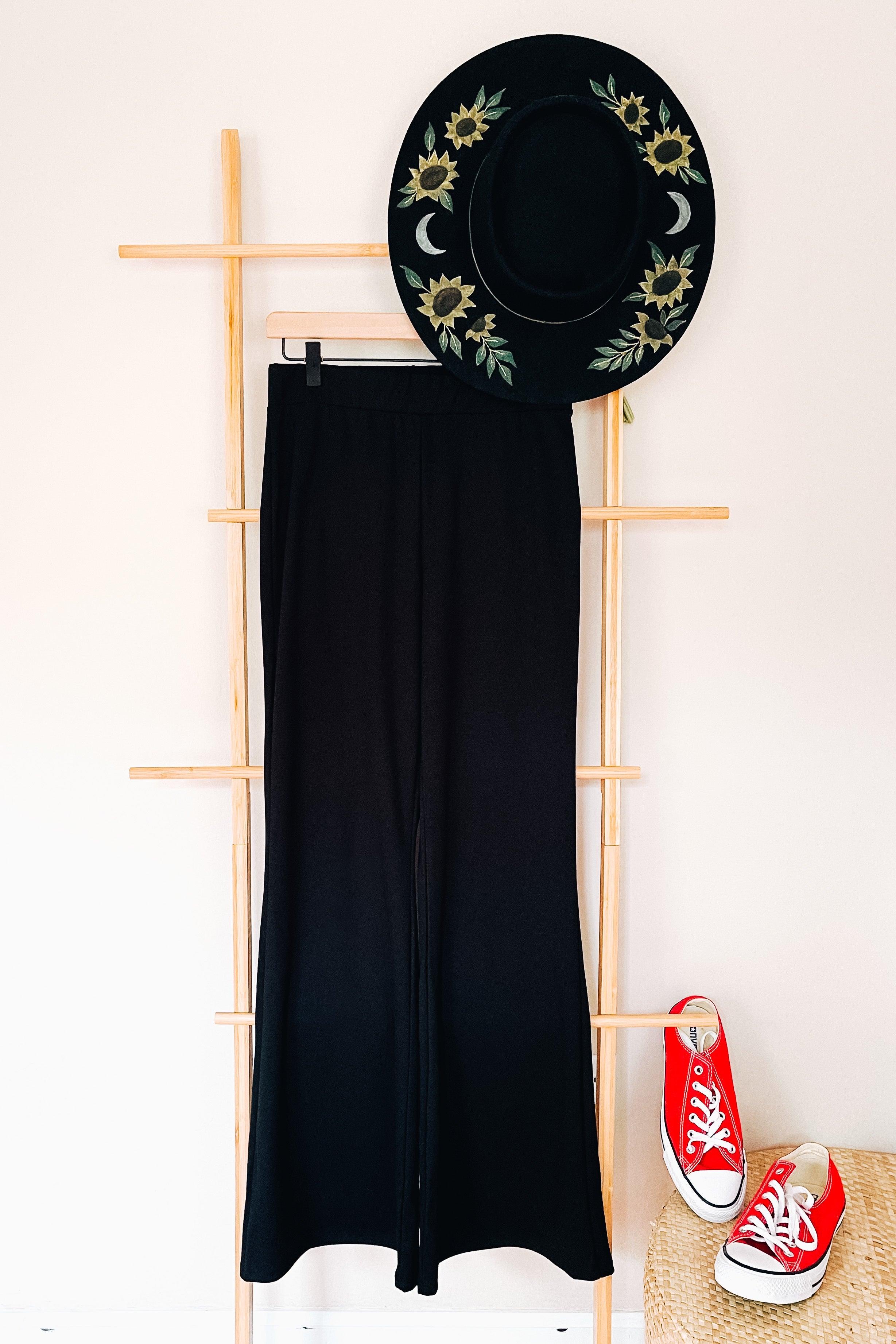 Black flared pants paired with embroidered black hat and vibrant red canvas sneakers on neutral backdrop