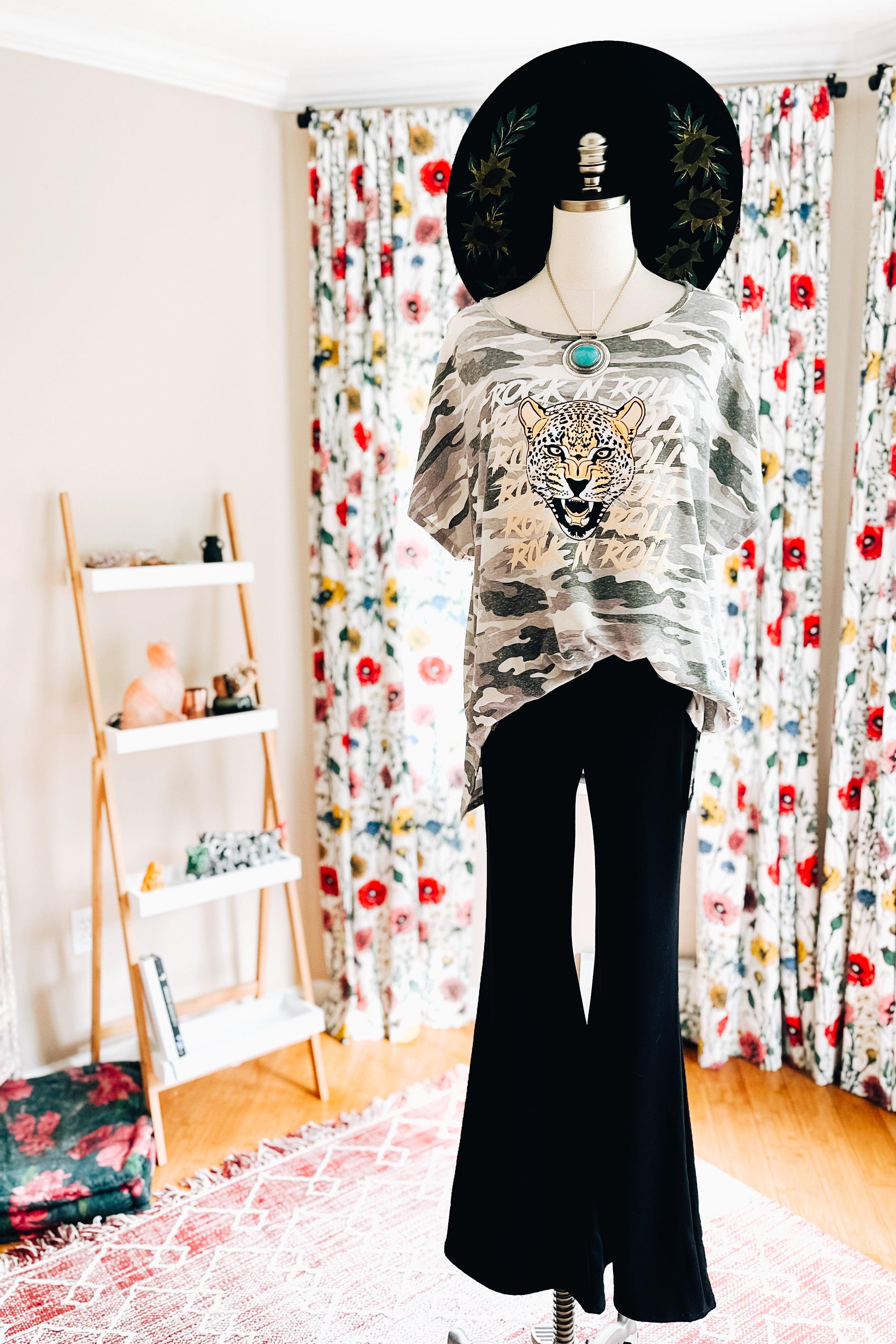 Mannequin dressed in black flares with loose camo top featuring leopard print and turquoise pendant necklace by floral curtains