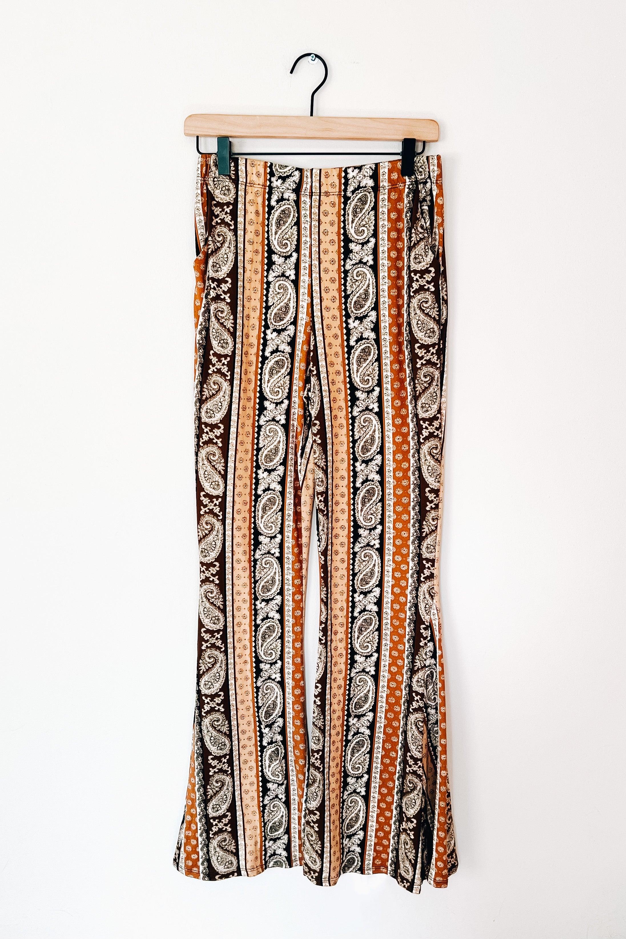 Rust striped paisley print flared pants hanging on wooden hanger against white background with eclectic bold style